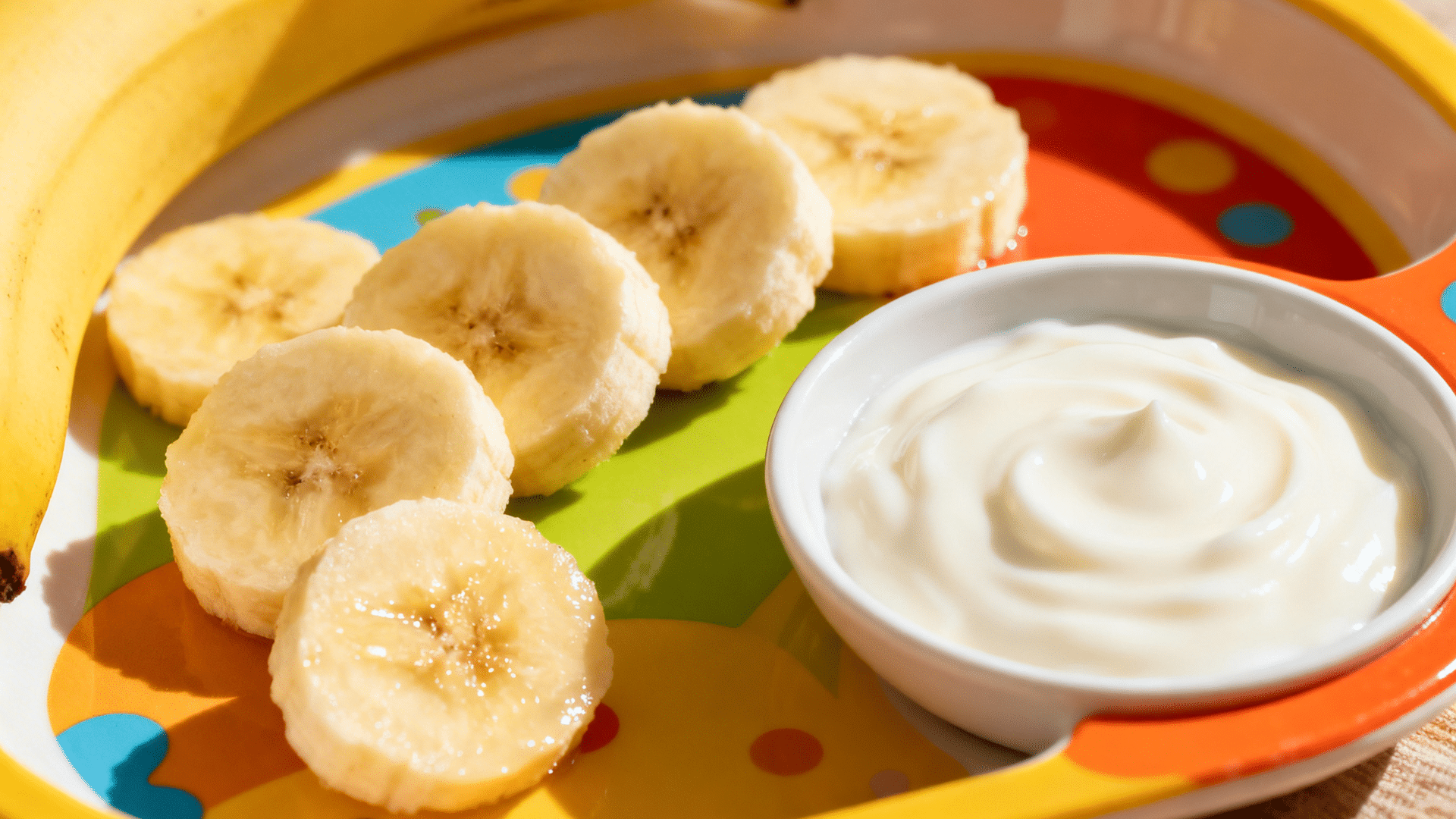 banana slices arranged on colorful plate with creamy yogurt dip and whole banana placed beside in bright light