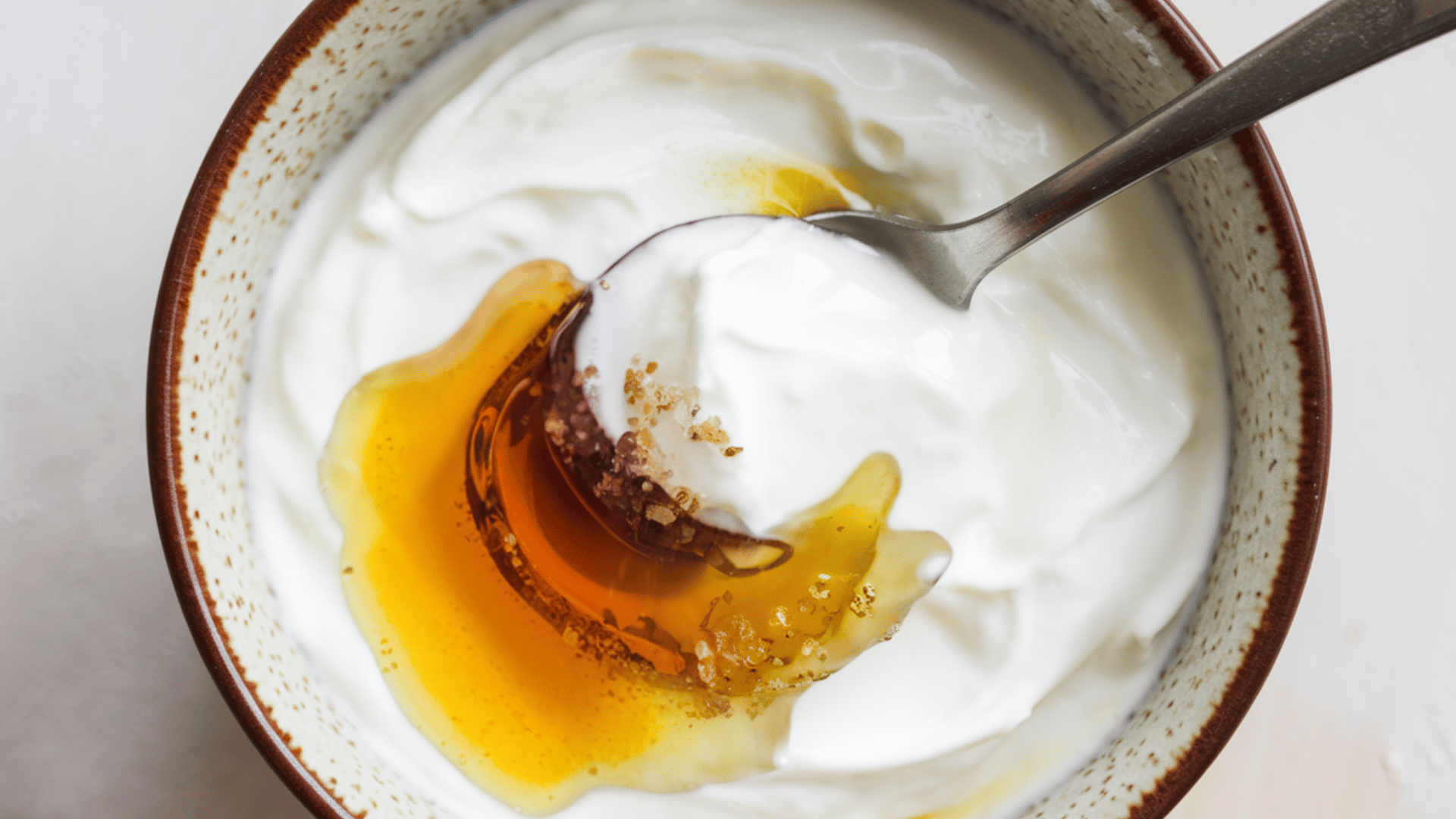 bowl of yogurt topped with honey being stirred with a spoon.