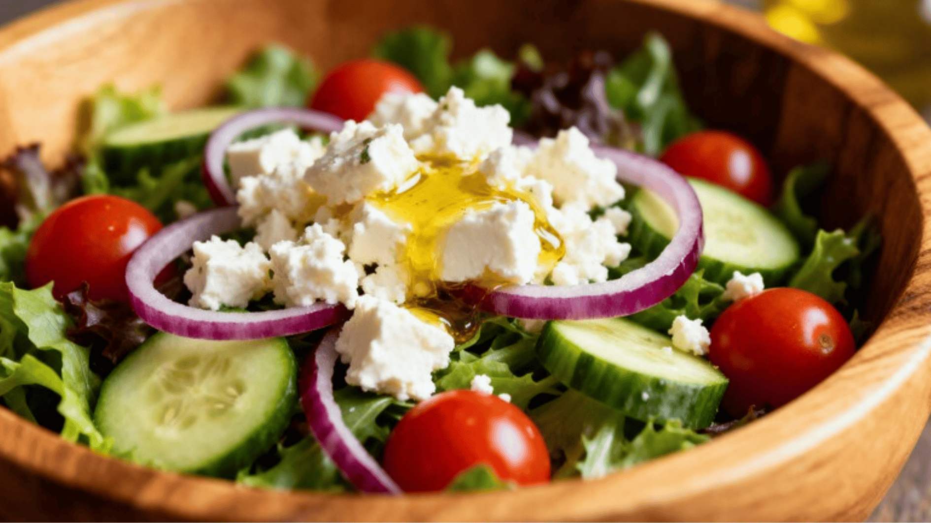 fresh Greek salad with cucumbers, cherry tomatoes, red onion, feta cheese, and olive oil served in wooden bowl on table