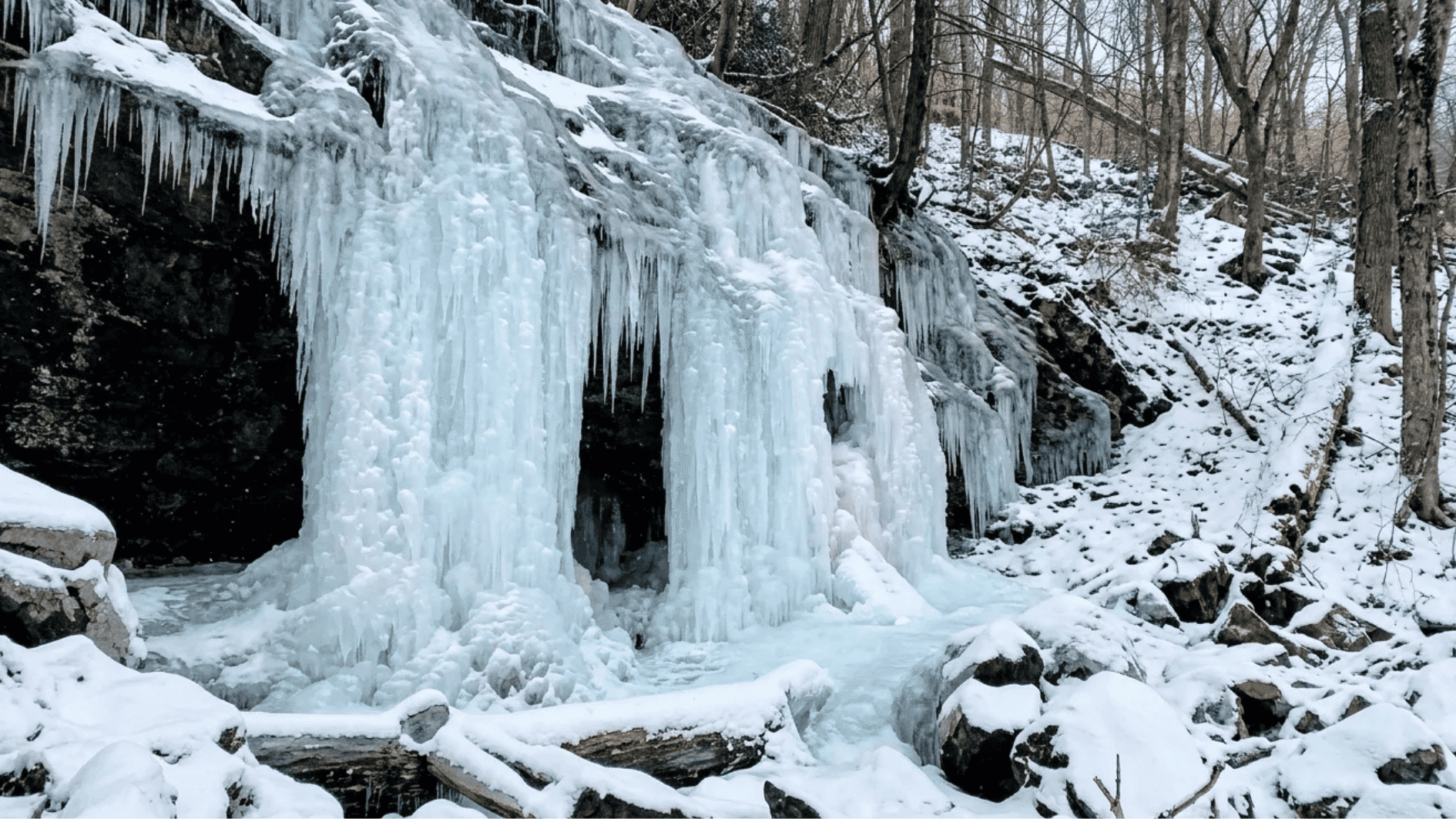frozen waterfall covered in thick ice and snow surrounded by rocks and trees in a quiet winter forest setting