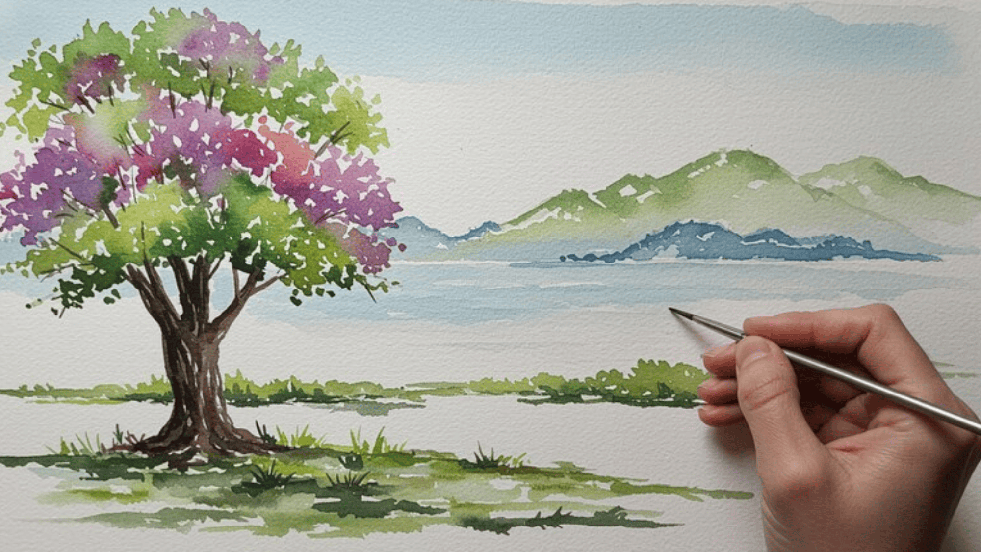 hand painting a watercolor landscape with a blooming tree, mountains, and lake on textured watercolor paper