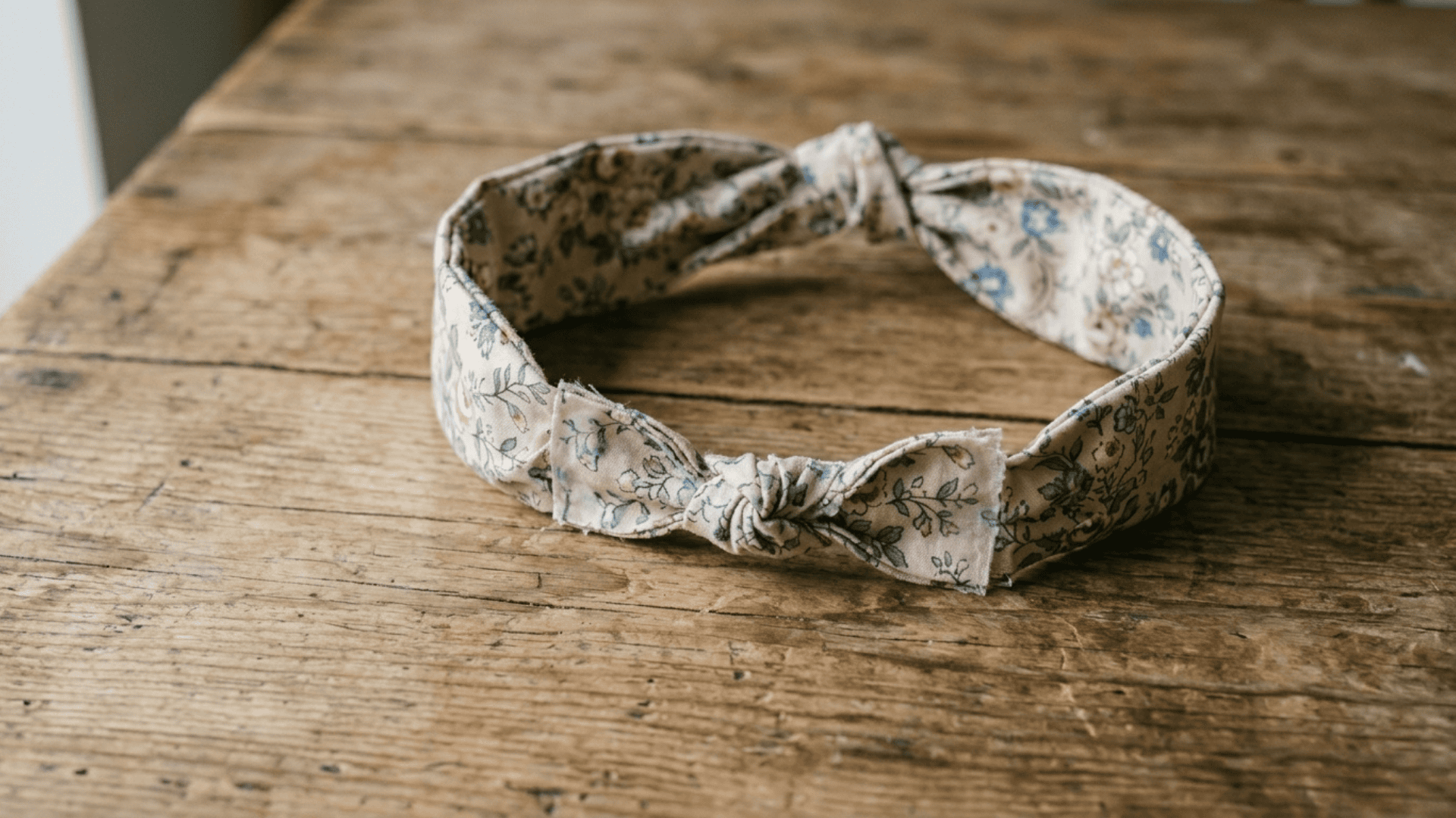 no-sew fabric headband made from floral cotton strip with knotted ends lying on a wooden surface as a diy gift for mom