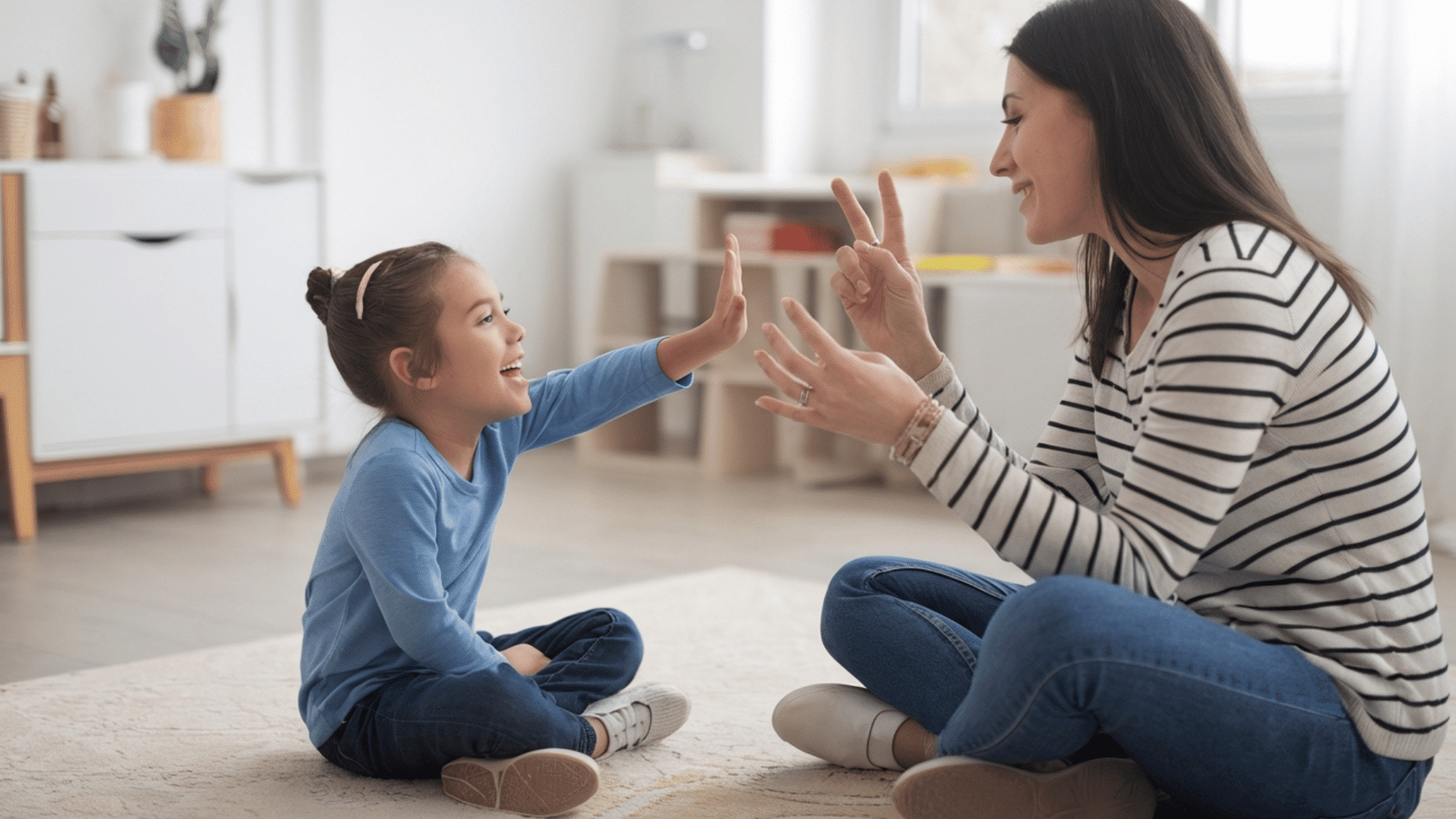 parent and child sitting on a rug using hand gestures to communicate specific instructions.