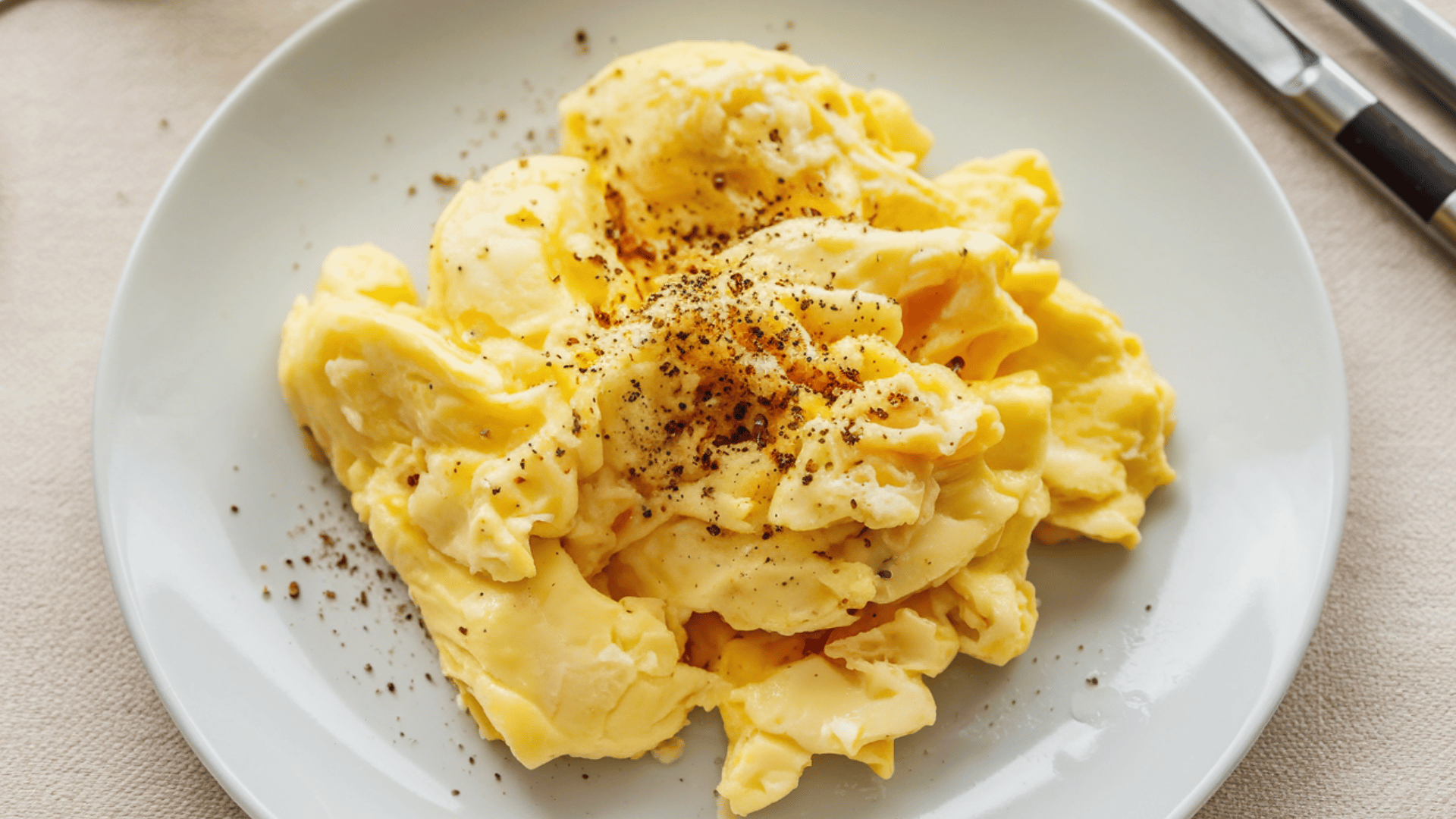 plate of soft scrambled eggs topped with black pepper on a white dish.