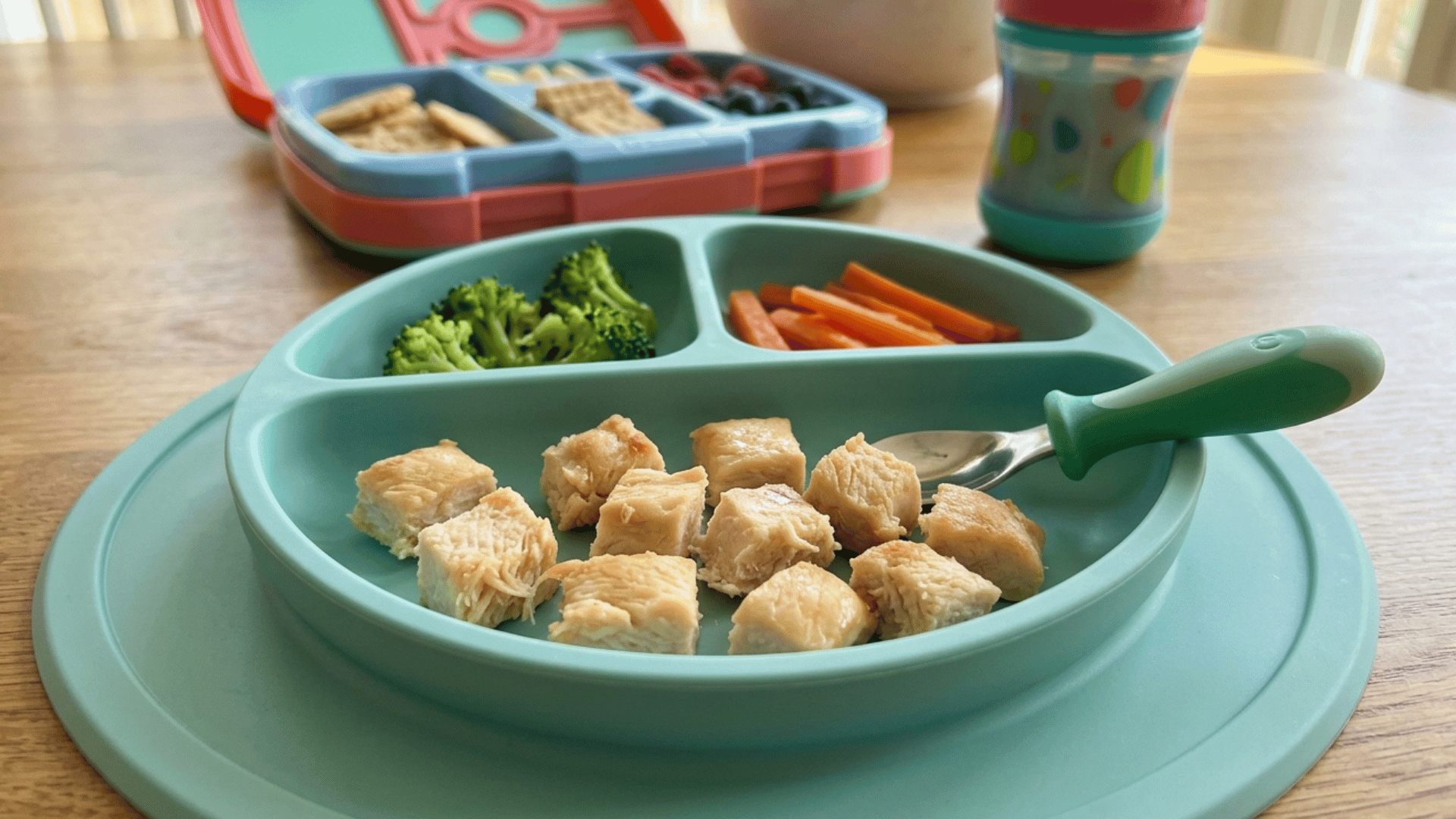 plate with small chicken pieces, broccoli, and carrots with spoon on a baby tray.