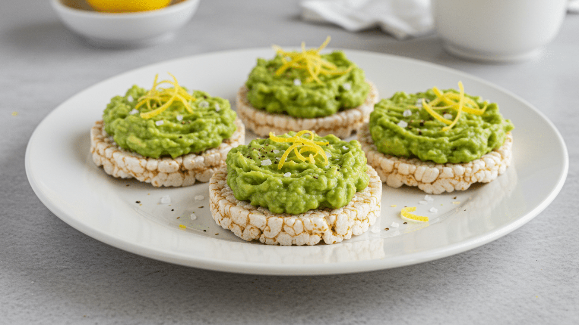 rice cakes topped with mashed avocado and lemon zest arranged on plate with simple clean background and soft lighting