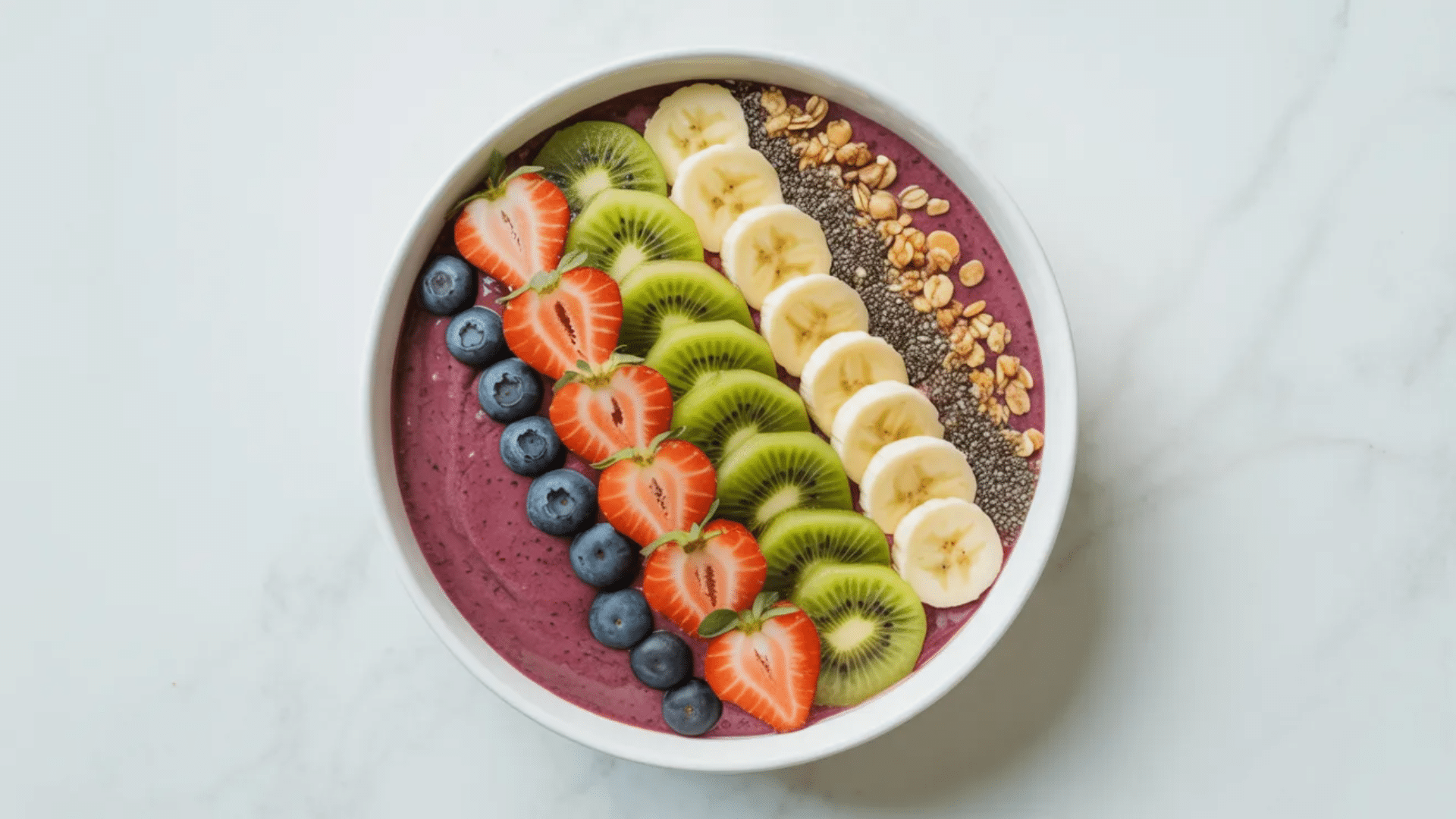 smoothie bowl topped with strawberries, kiwi, banana, blueberries, granola, and chia seeds