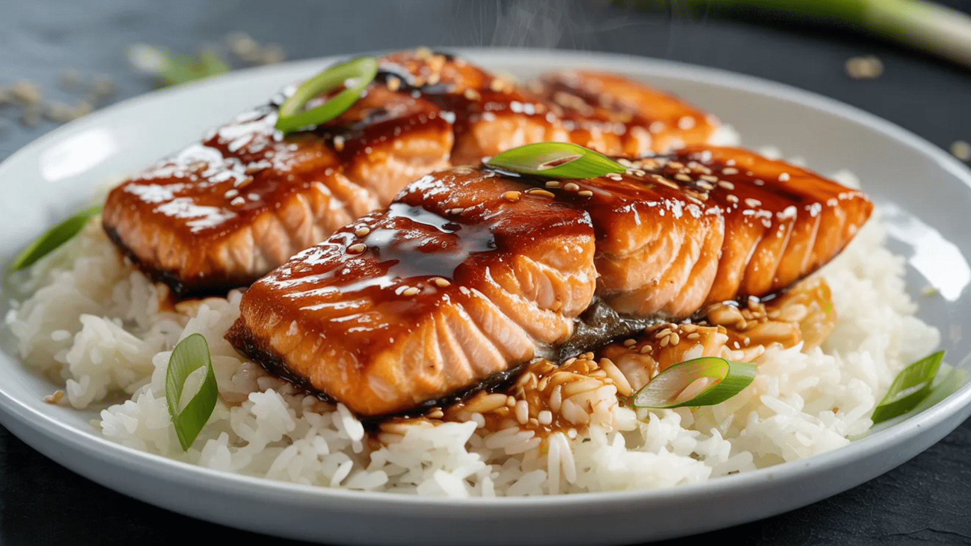 teriyaki glazed salmon fillets served over white rice garnished with sesame seeds and green onions on a plate