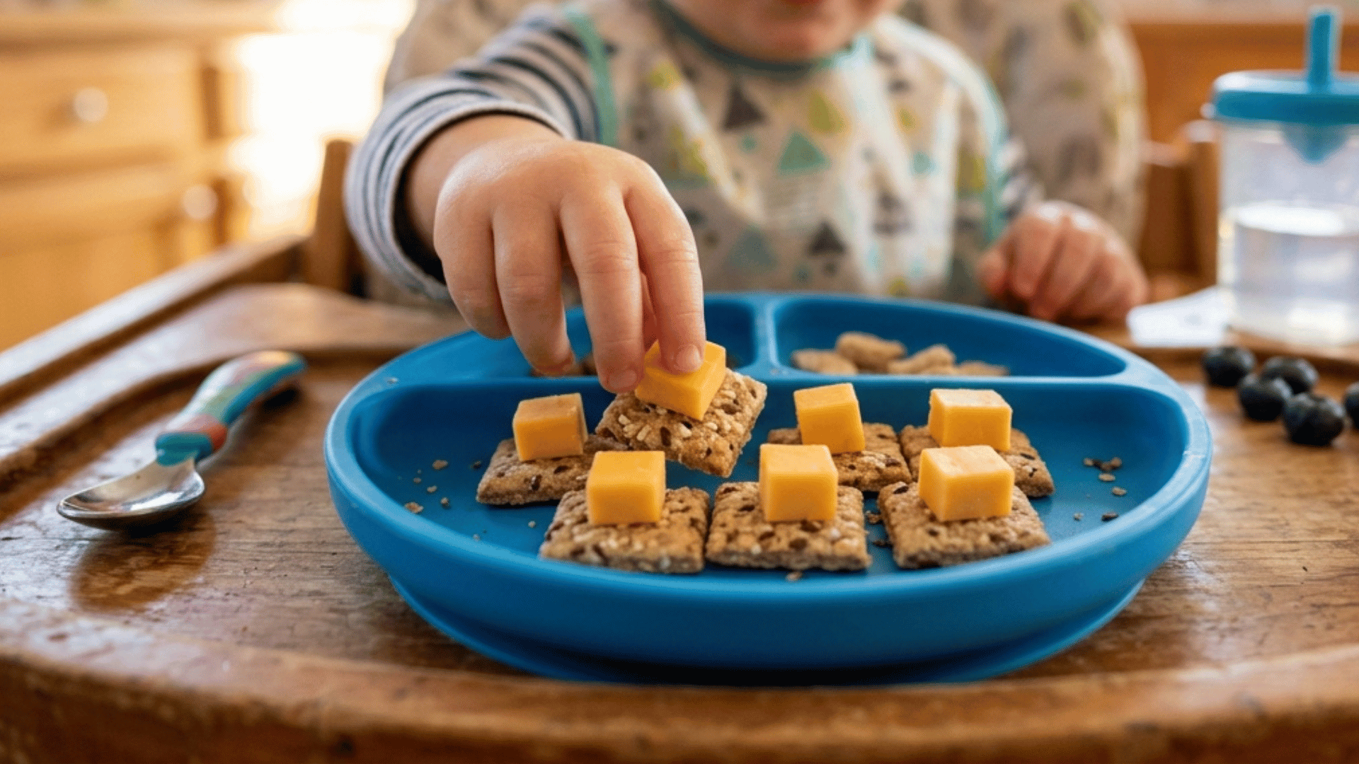 toddler picking cheese cubes from whole grain crackers on a divided plate.