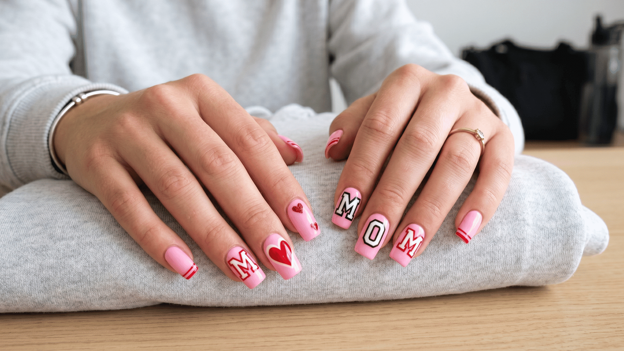 varsity mom nail design with pink base bold lettering and heart accents