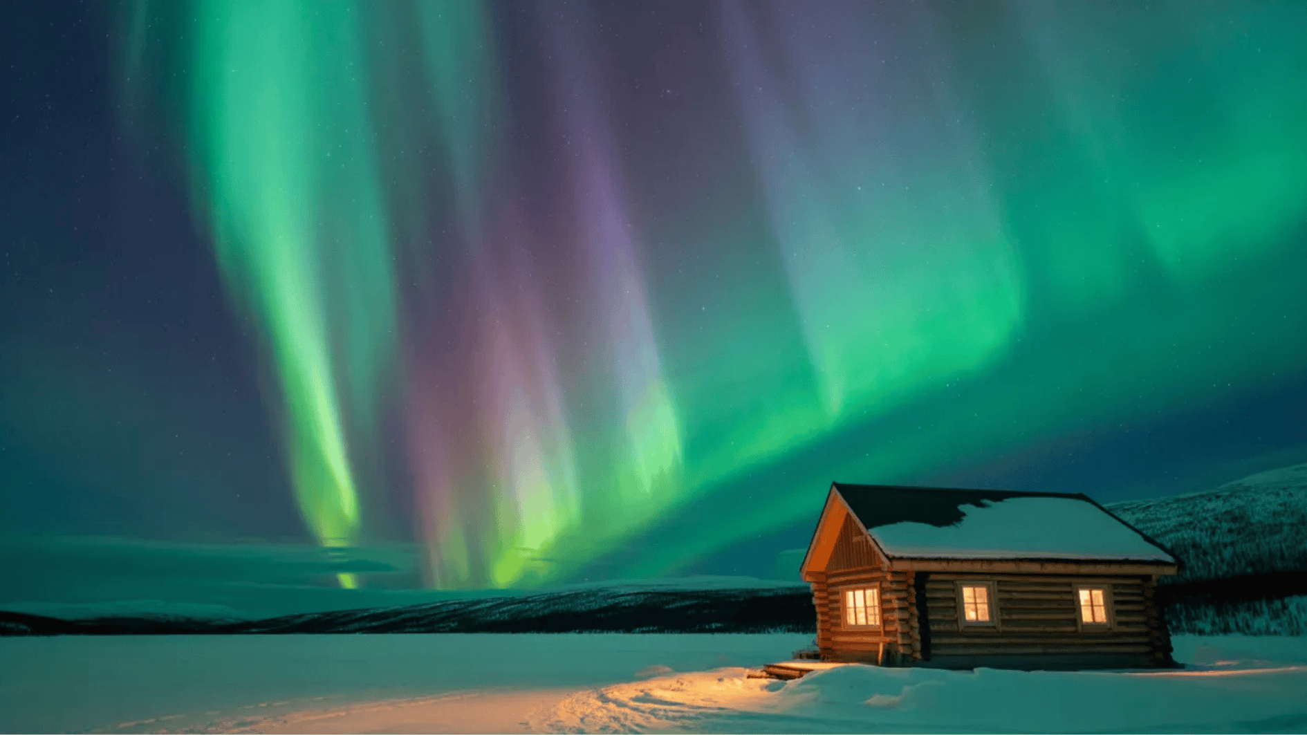 vivid green and purple northern lights display fills the night sky above a snow-covered landscape, a small wooden cabin with warm