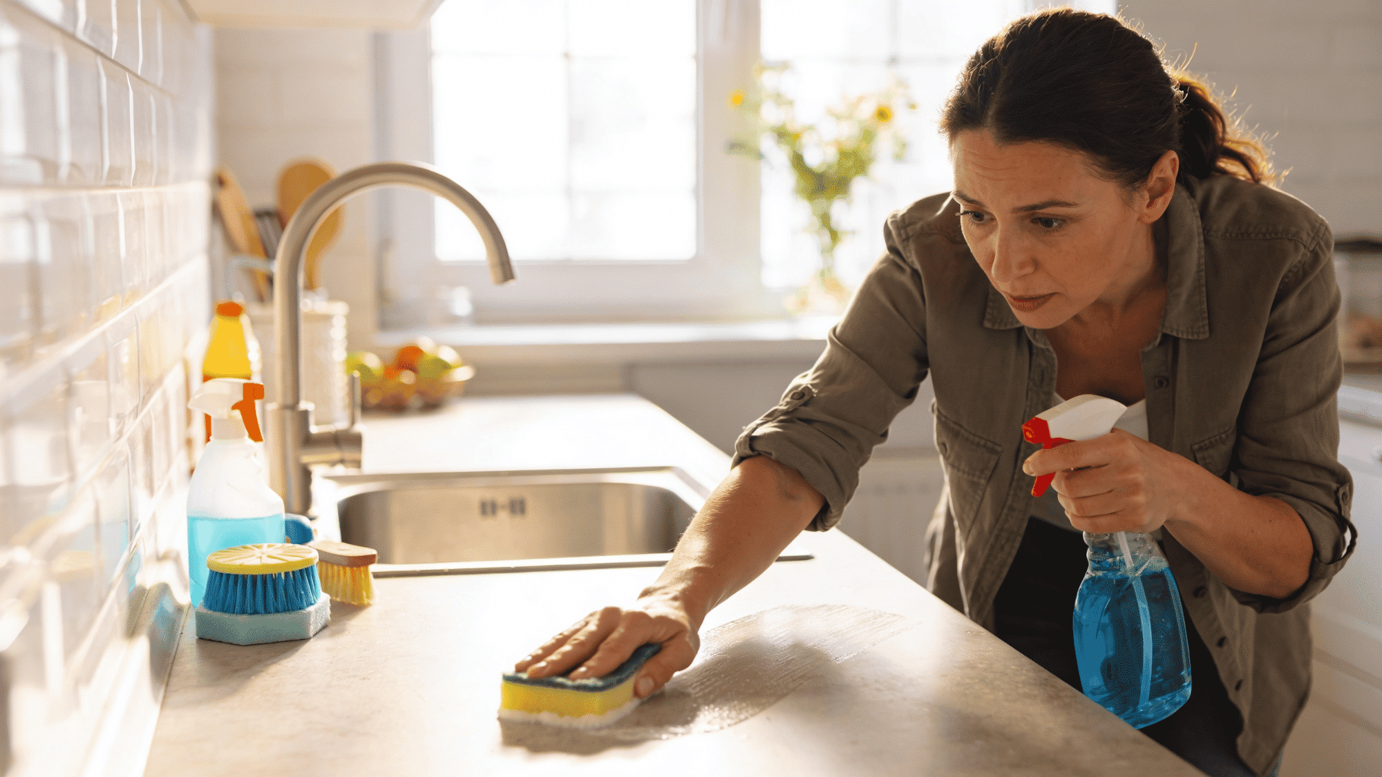 adult woman deep cleaning kitchen countertop with sponge and spray bottle in natural light