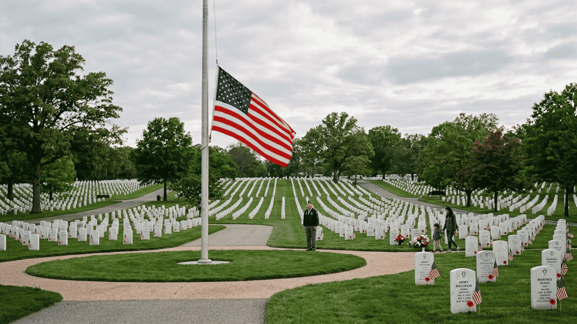 american flag at half-staff in a military cemetery with white headstones on memorial day