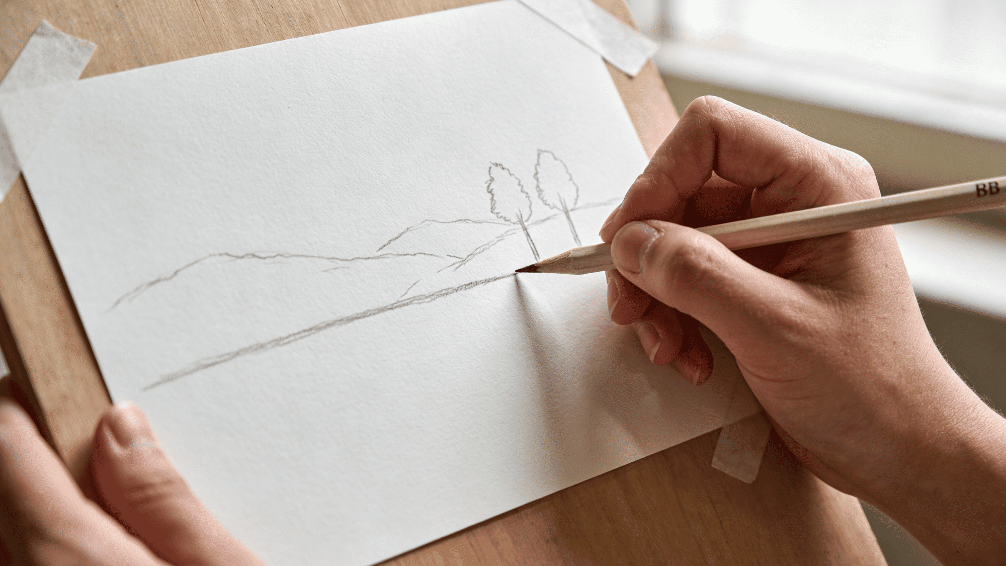 artist sketching landscape with pencil on paper at wooden easel in natural daylight