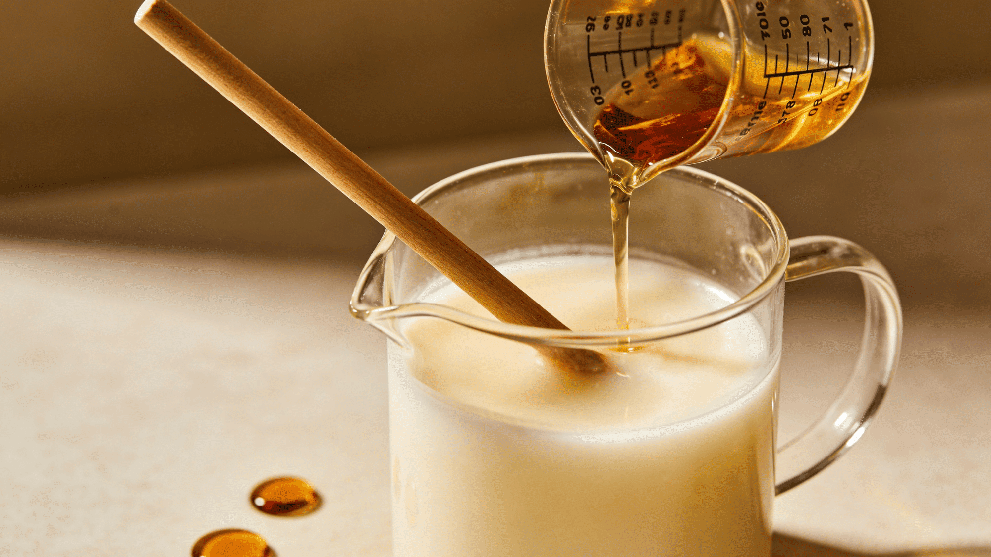 fragrance oil being poured into melted soy wax in a pitcher with candle dye and a wooden stirring stick nearby.