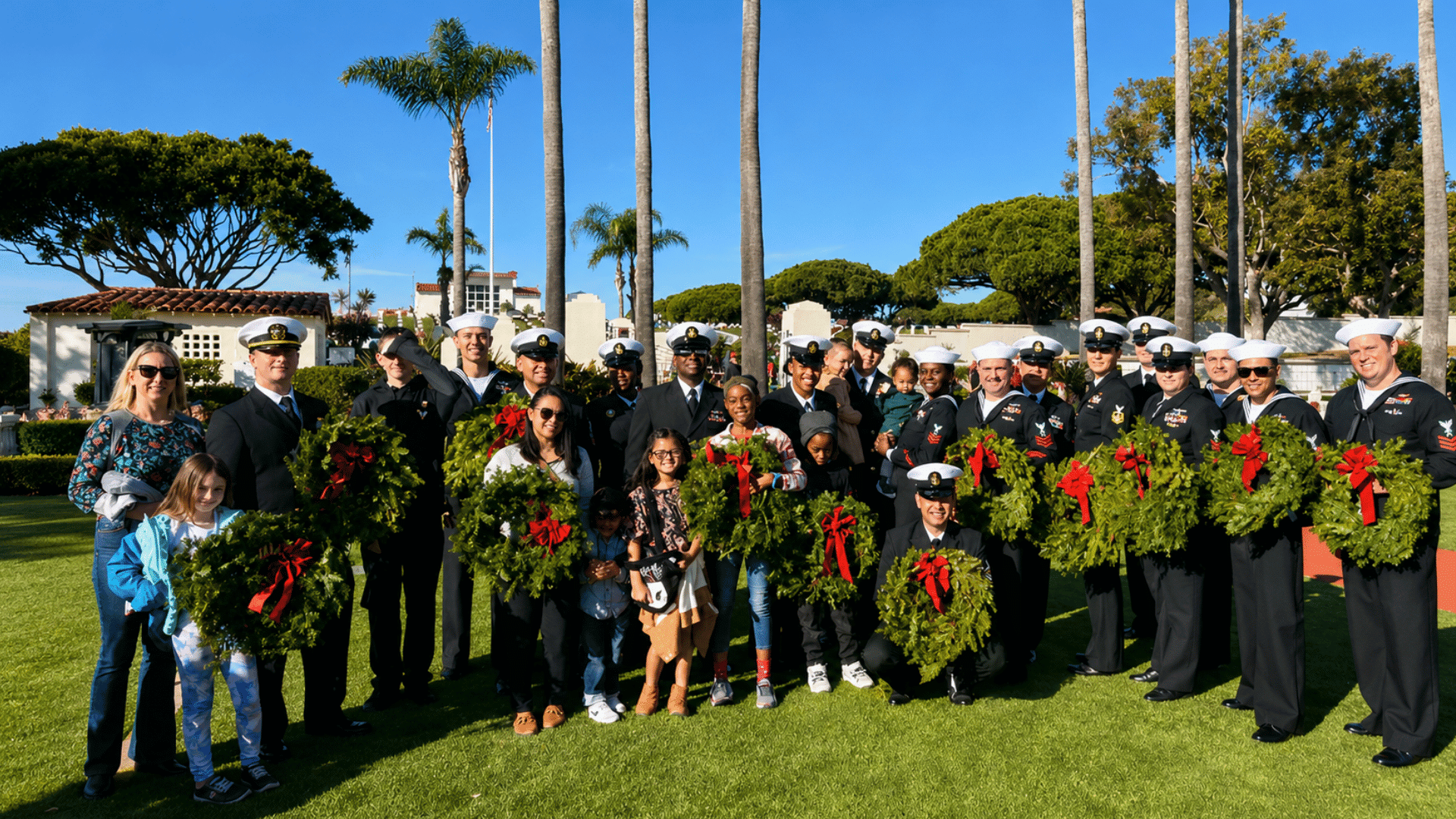 military members and families holding wreaths during a memorial day ceremony under bright blue skies (1)