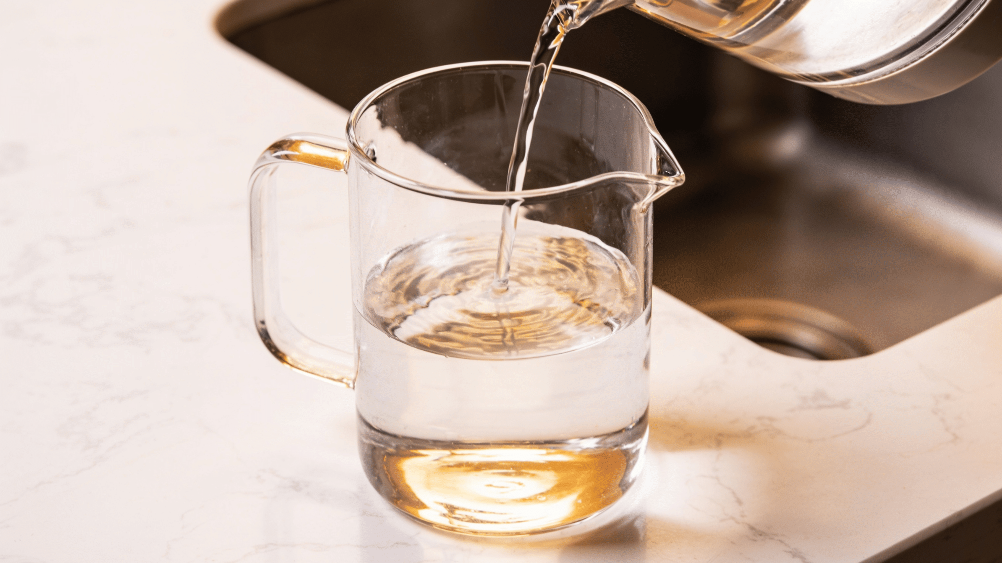 _a glass pitcher filled with warm water on a white marble counter for making diy flower food at home