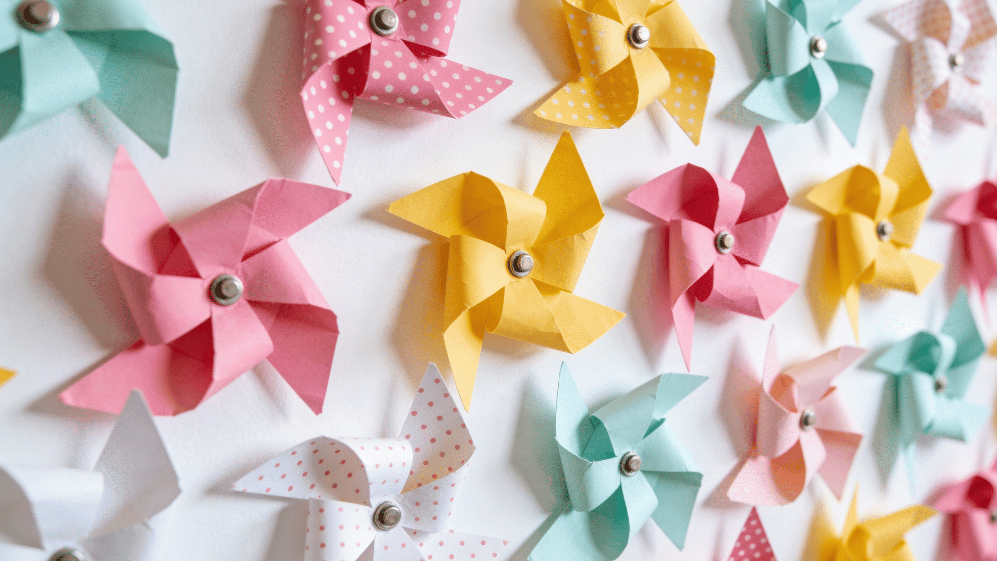 backdrop board covered in handmade paper pinwheels in pink yellow mint and white patterns on a white wall