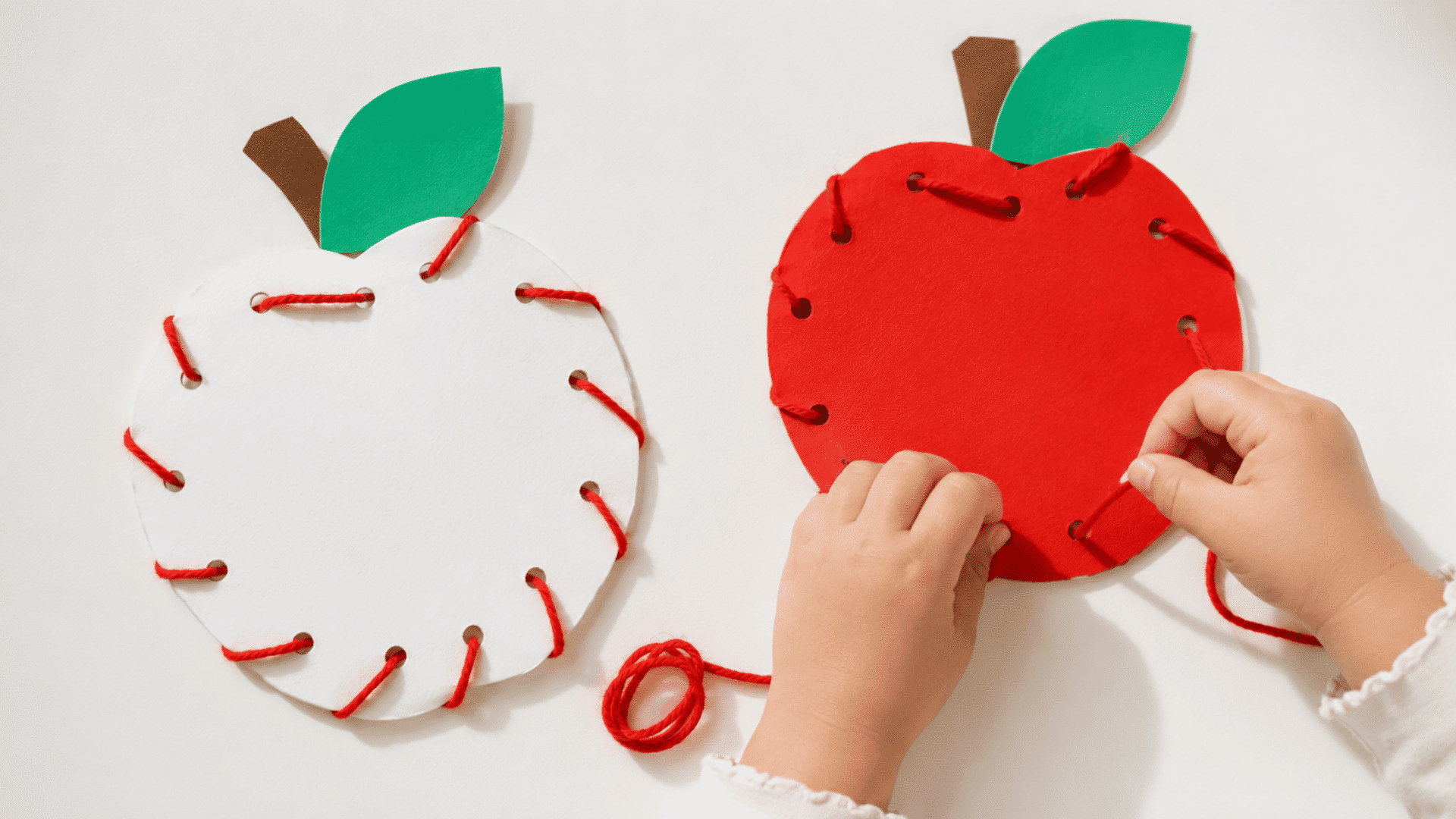 childrens lacing apple craft activity red and white color apples being laced by red woolen thread by a toddlers hand visible bright light and shadow