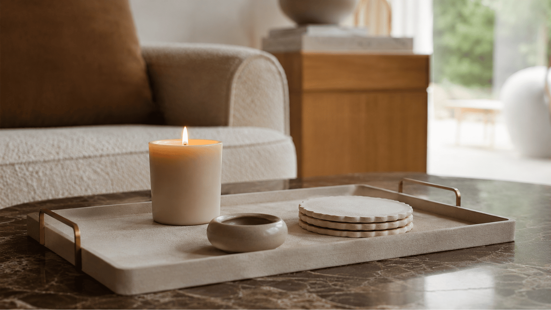 Decorative tray with a lit candle and scalloped coasters on a dark marble coffee table