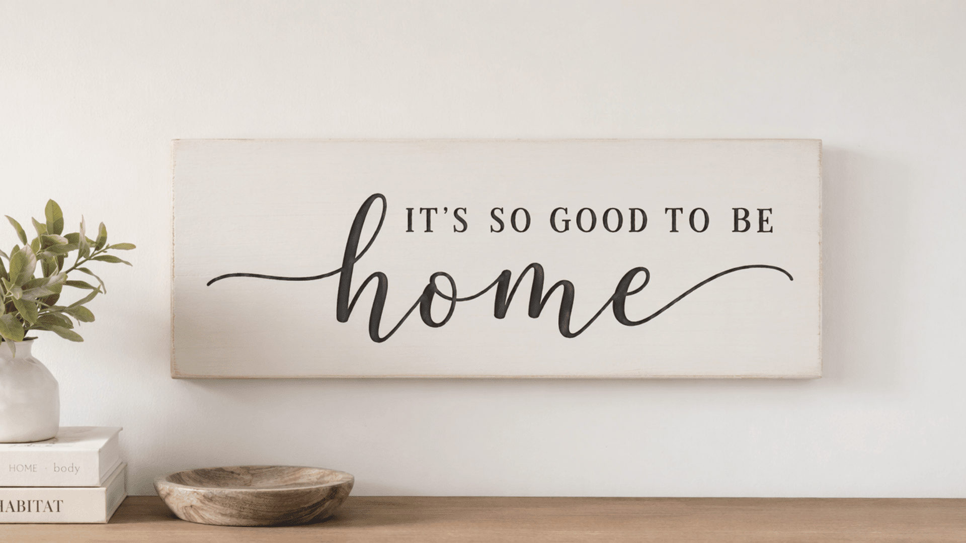 finished painted wooden wall sign with clean hand-lettered text, simple wood board with smooth painted surface, placed on a plain light-colored home wall, minimal home decor style
