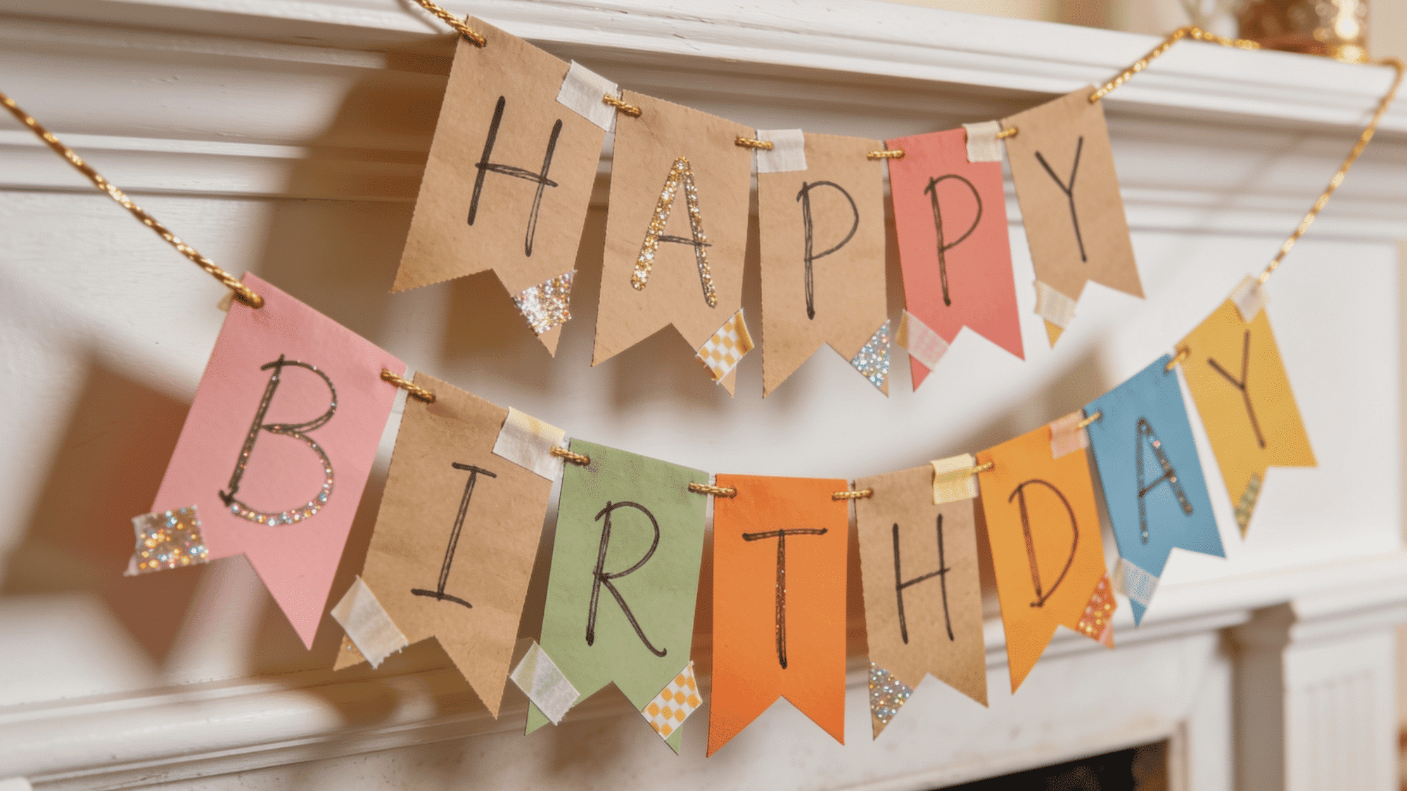 handmade kraft paper birthday pennant banner with washi tape and glitter strung on gold twine on a mantle