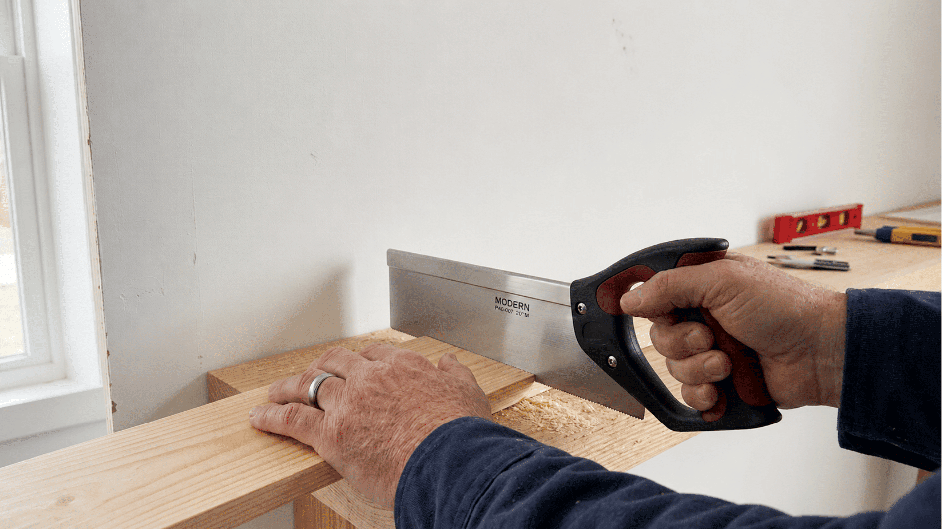 Hands using a hand saw to cut pine lumber to size on a workbench.