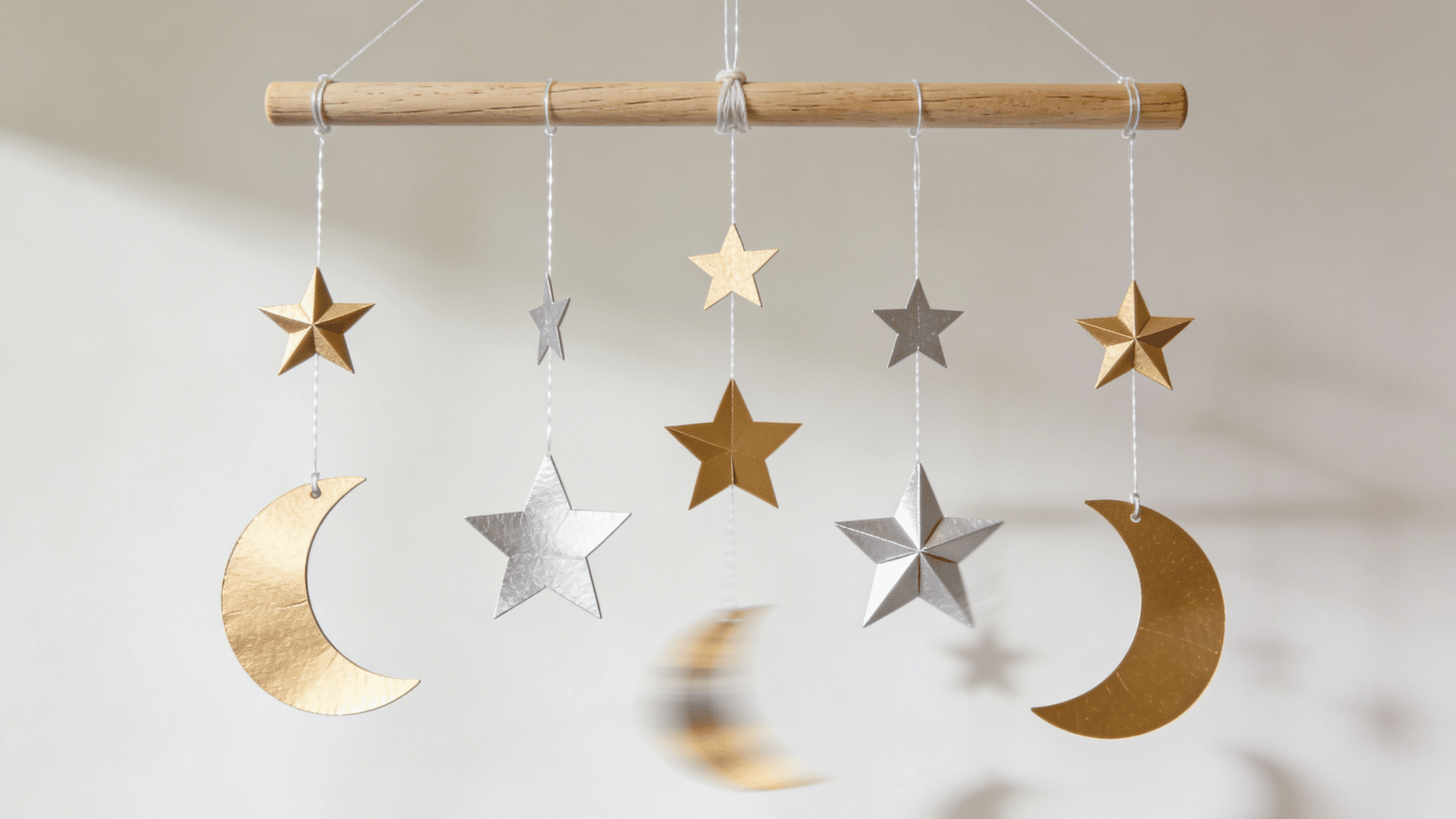 hanging ceiling mobile with gold and silver cardstock stars and moons on fishing line tied to a wooden dowel