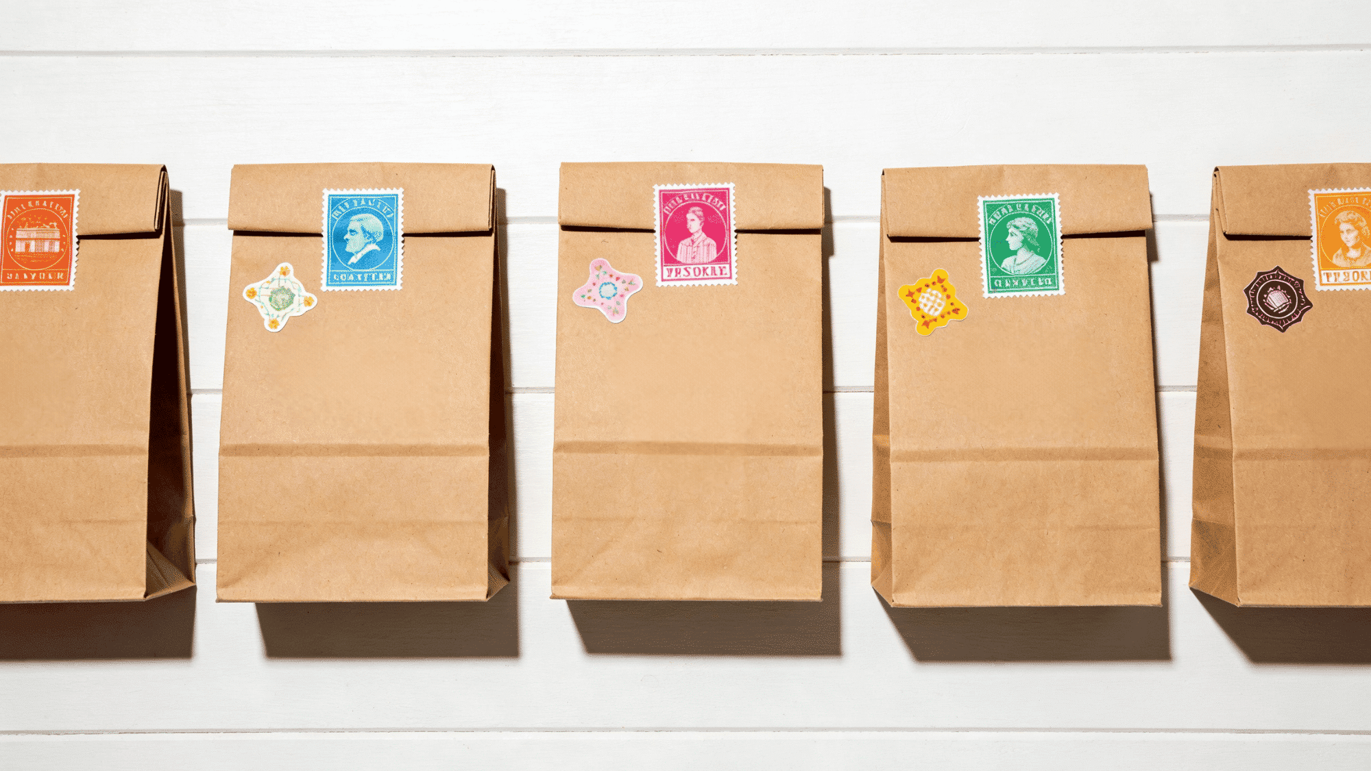 kraft paper birthday favor bags with colorful stamps and handwritten names arranged neatly on a white tabl