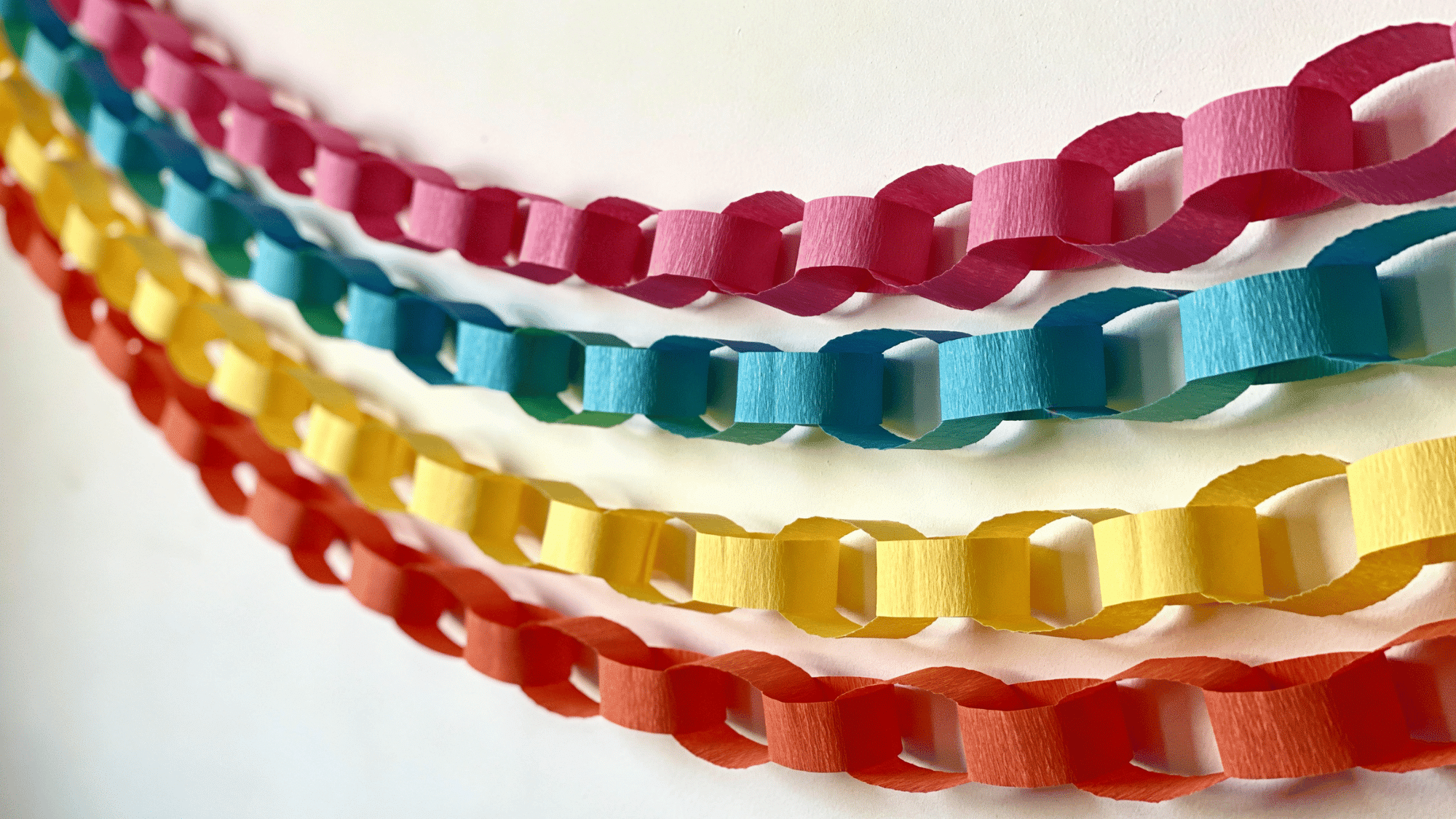 long rainbow paper chain garland hung across a white wall in gentle loops as colorful birthday party decor