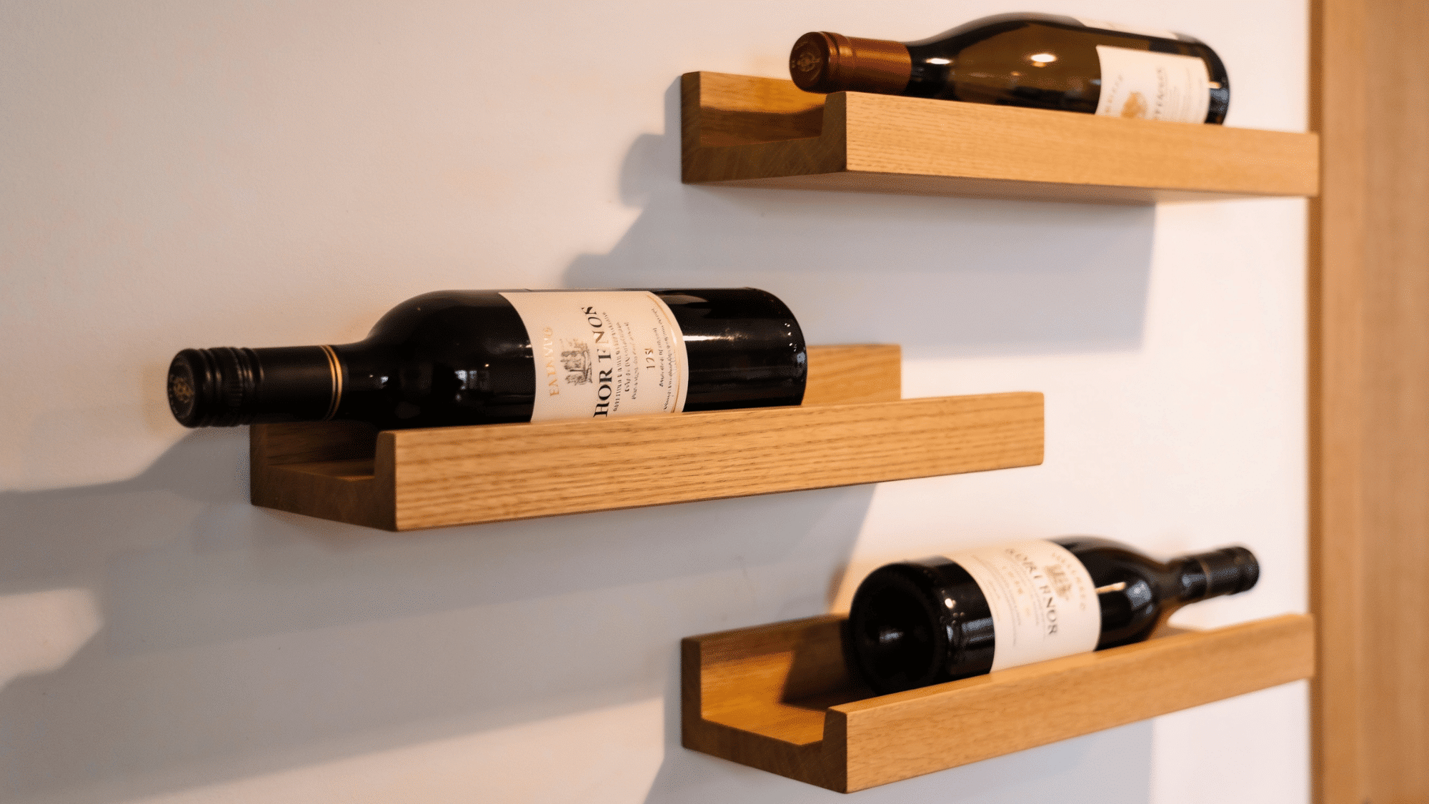 minimal floating wood shelves on white wall holding wine bottles horizontally soft ambient light