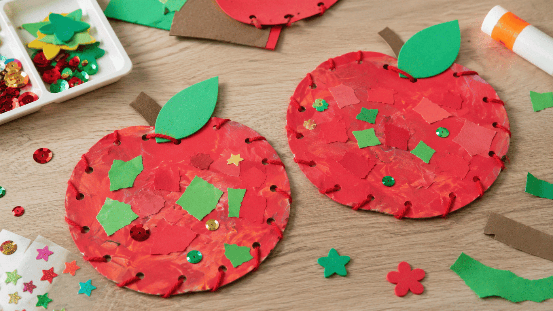photo of a apple collage craft use paper scraps, foam pieces, stickers, and other craft bin items visible painted red green with craft materials nearby in an indoor setting