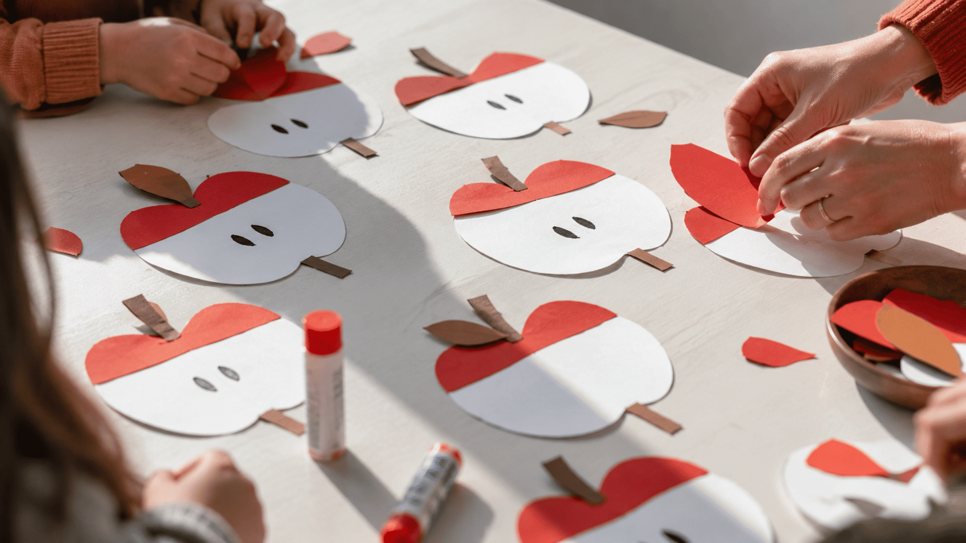 photo of a preschool craft table with apple core crafts, white apple core cutouts, red paper pieces for the top and bottom, brown paper stems, black marker seed marks