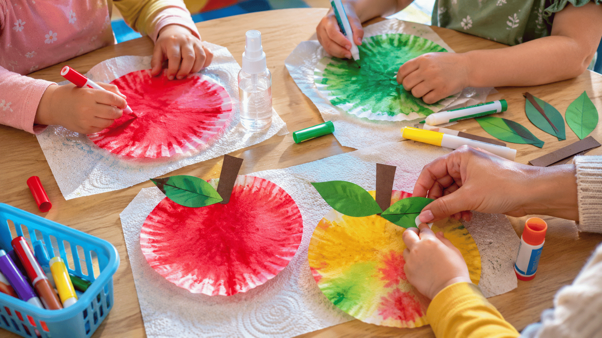 photo of a preschool craft table with coffee filter apple crafts, round coffee filters colored red, green, and yellow with washable markers, small spray bottle of water nearby