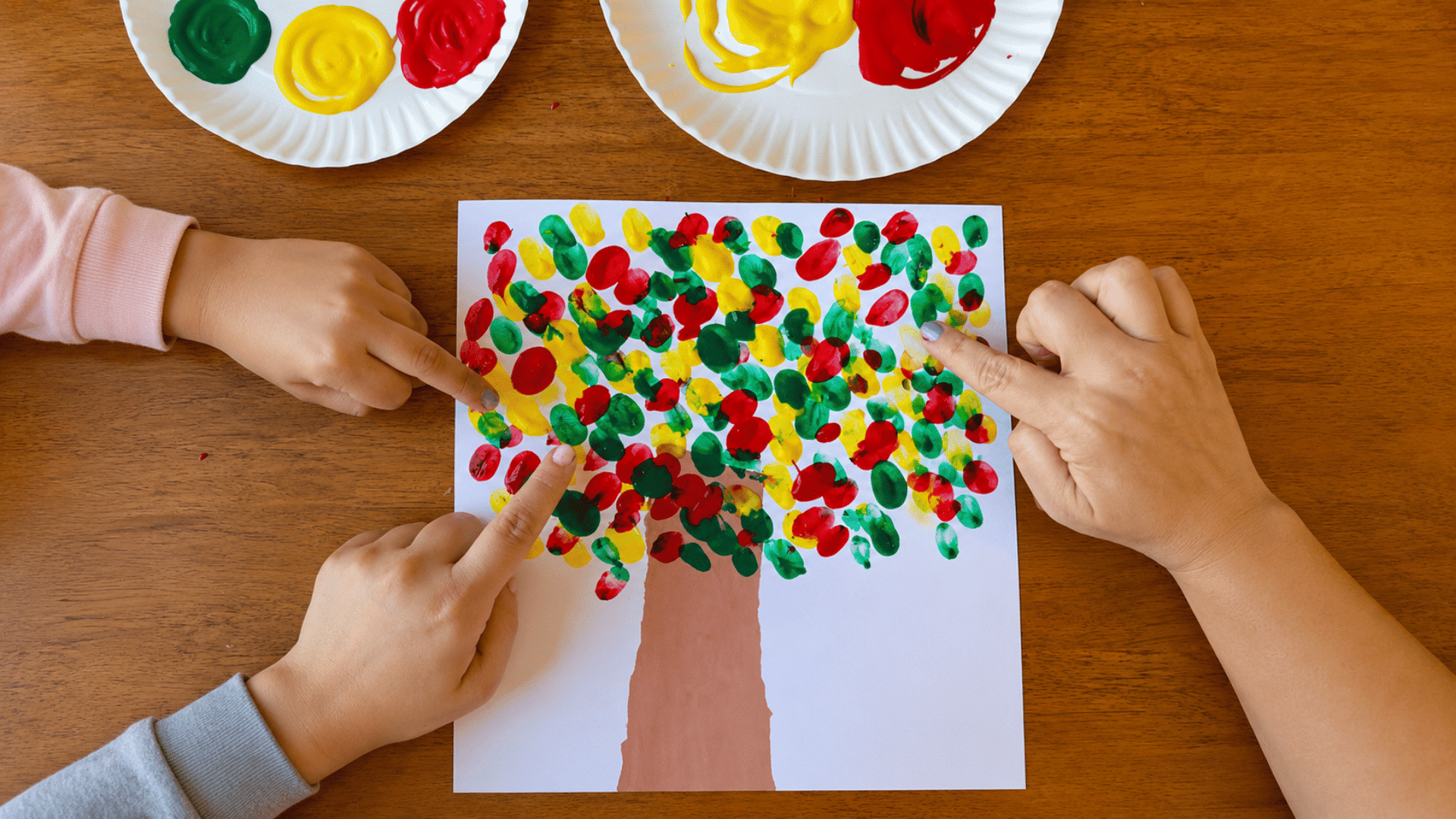 photo of a preschool craft table with fingerprint apple craft activity, white paper with apple tree outlines, red washable paint for fingerprint apples, green paint for leaves, brown painted tree