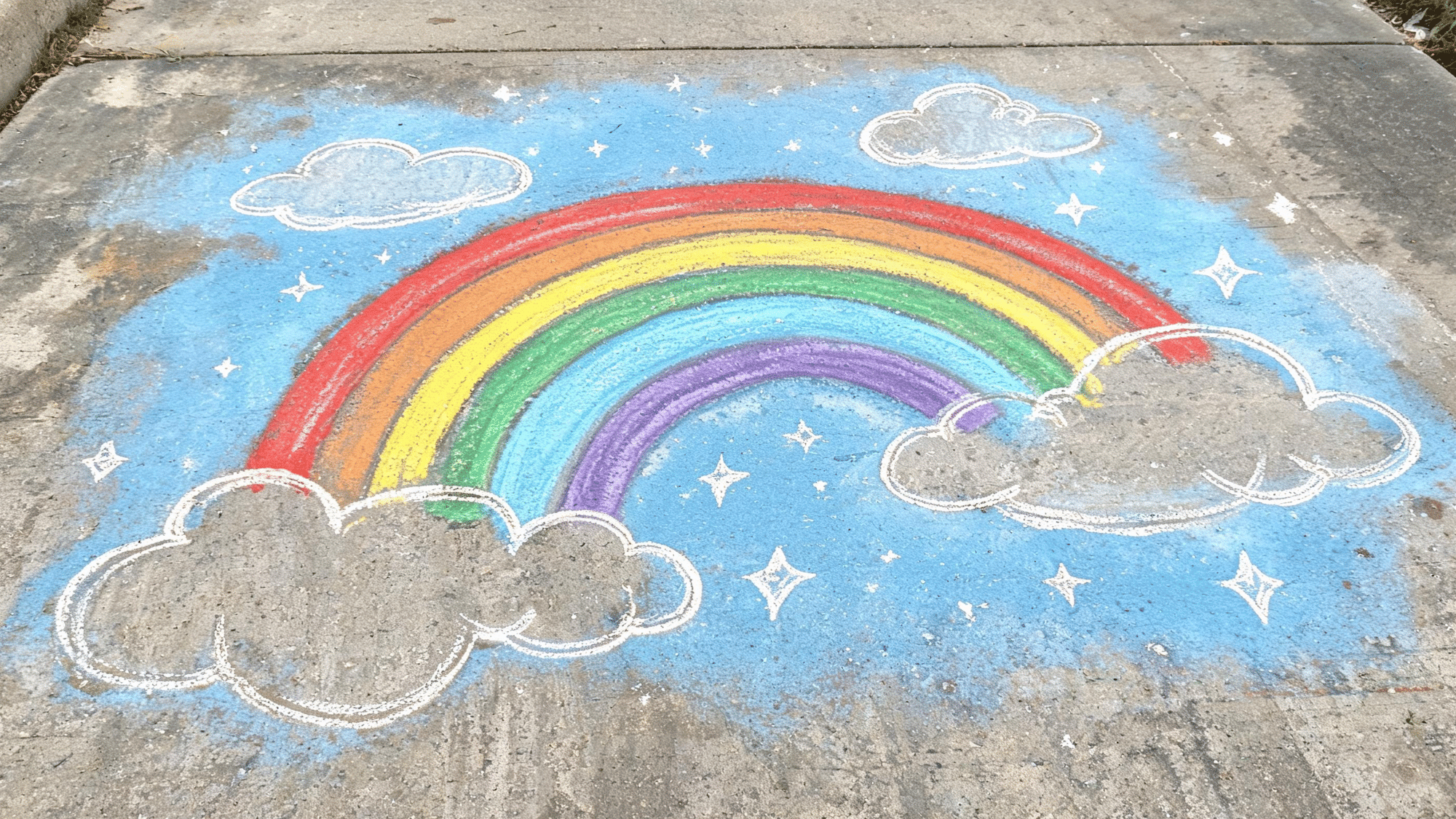 colorful sidewalk chalk art drawing of a large rainbow with bright curved bands