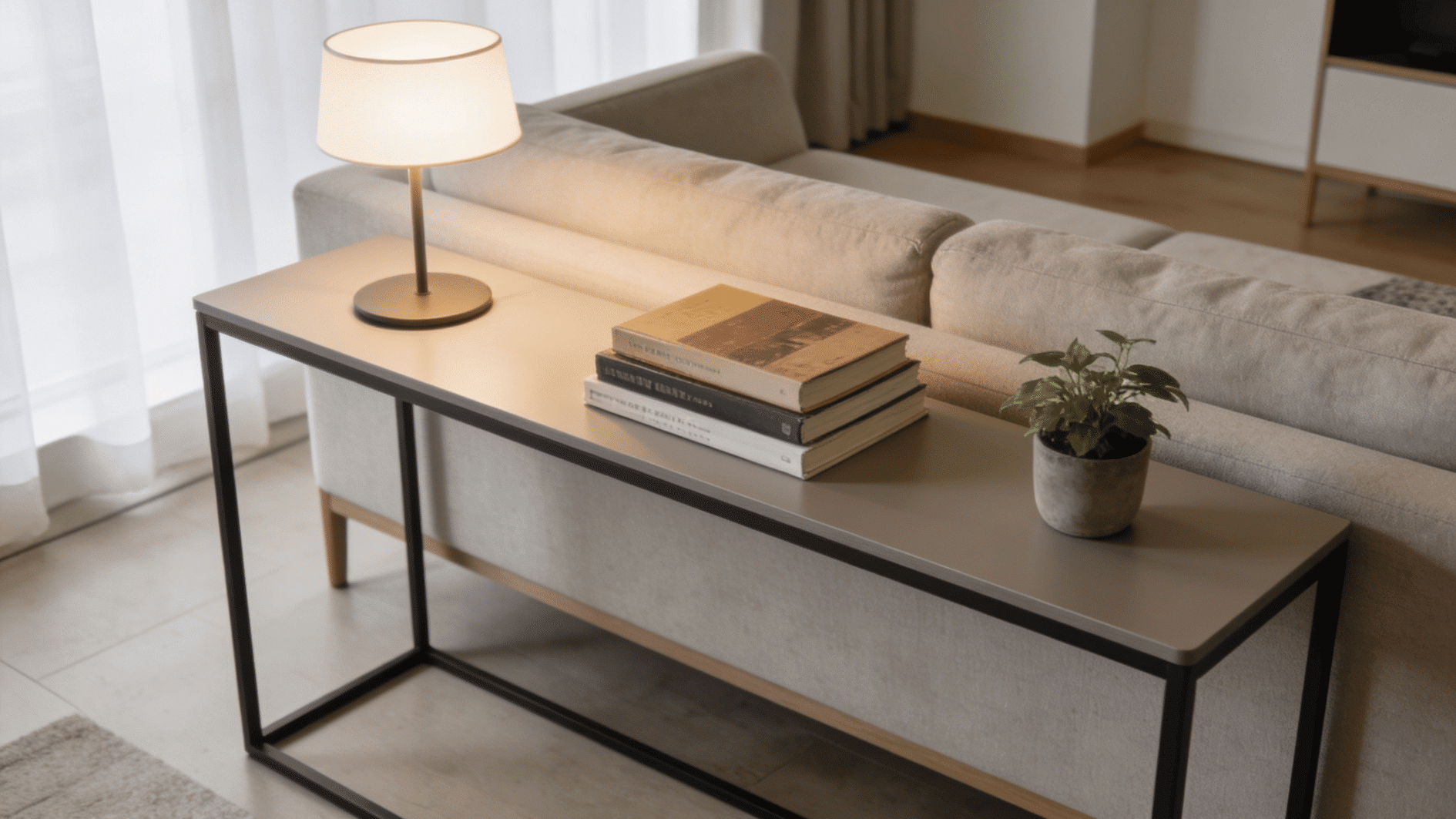 slim console table behind a sofa with lamp, books and a small potted plant