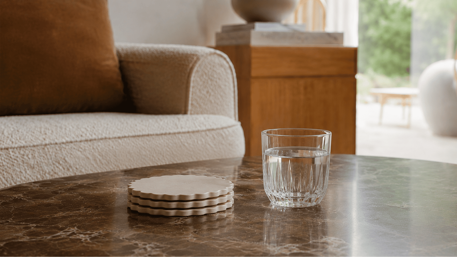 Stack of scalloped cream coasters beside a glass of water on a marble coffee table