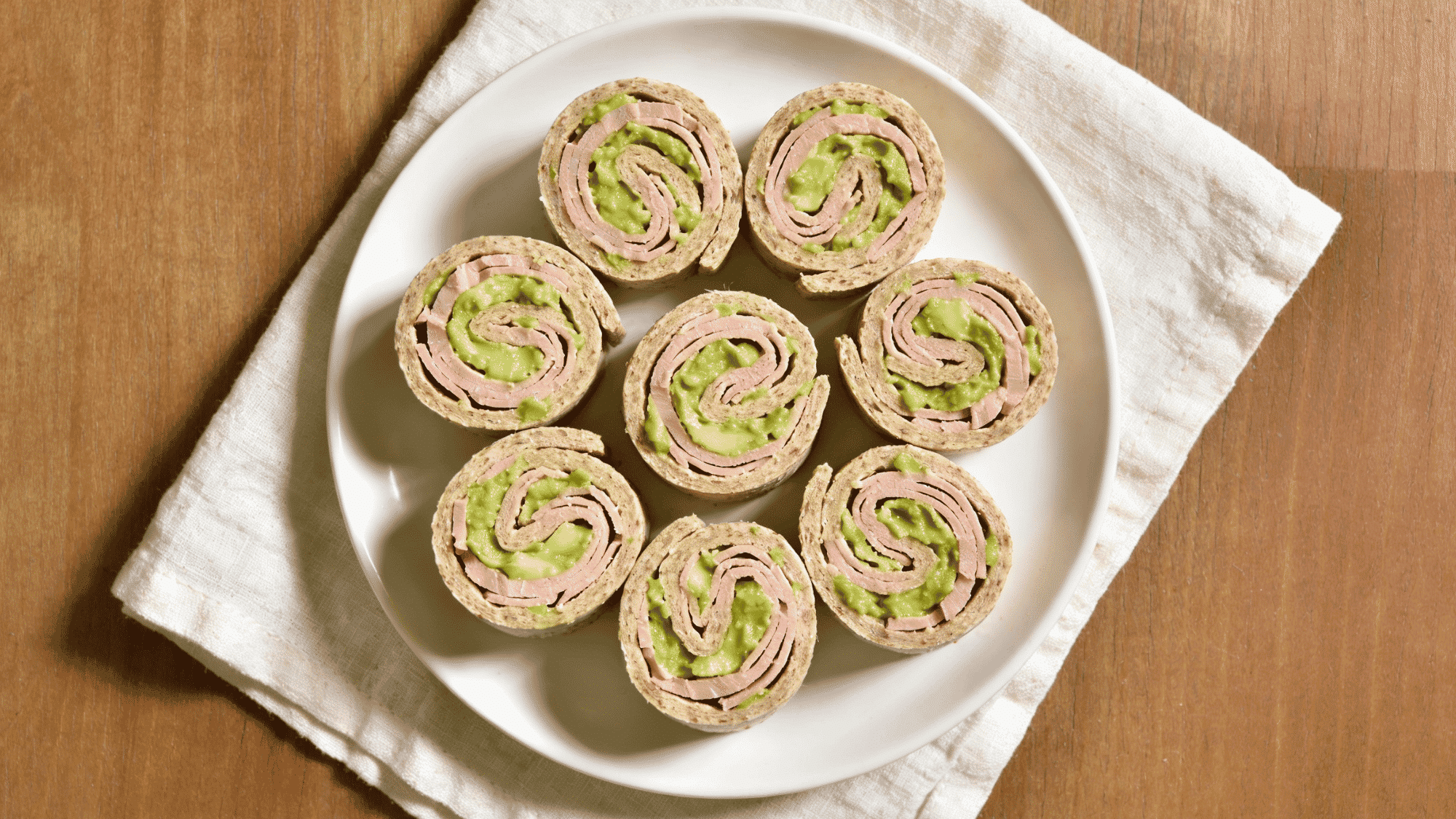 _turkey and avocado pinwheel slices on white plate with green swirl inside, healthy kids lunchbox meal idea