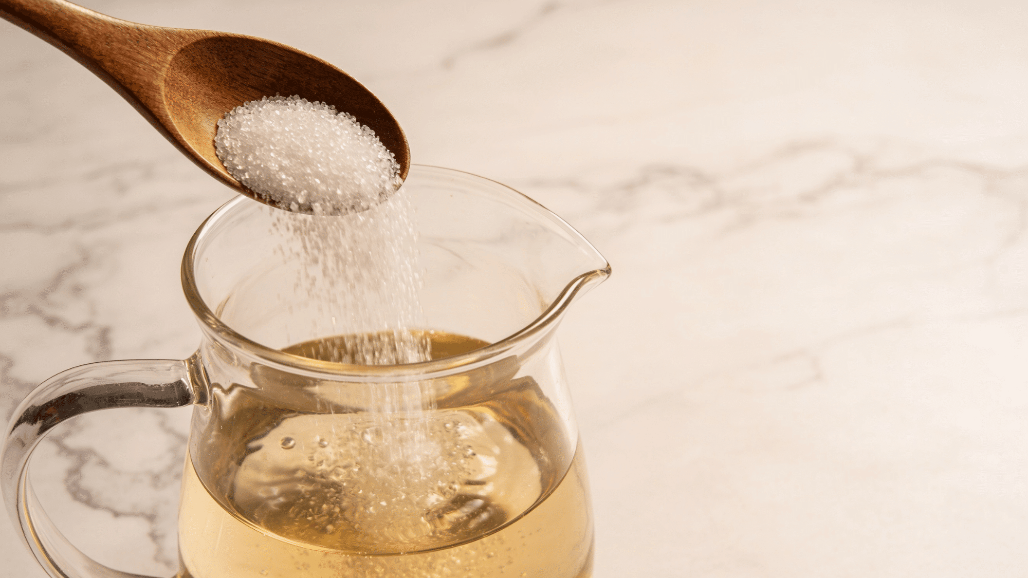 white sugar being stirred into warm water in a glass pitcher as part of a flower food diy recipe
