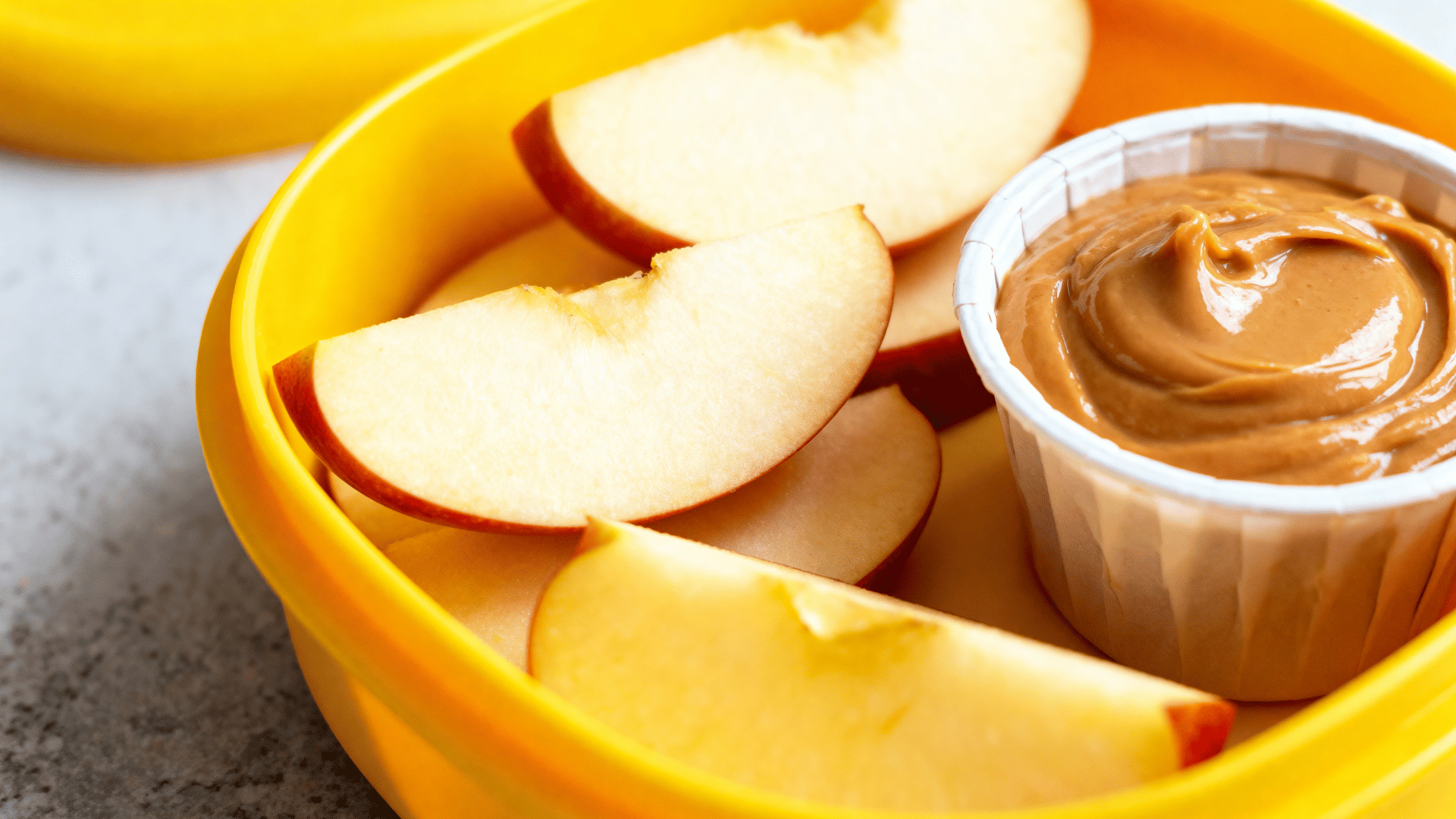 apple slices with peanut butter dip in a daffodil-yellow silicone lunchbox