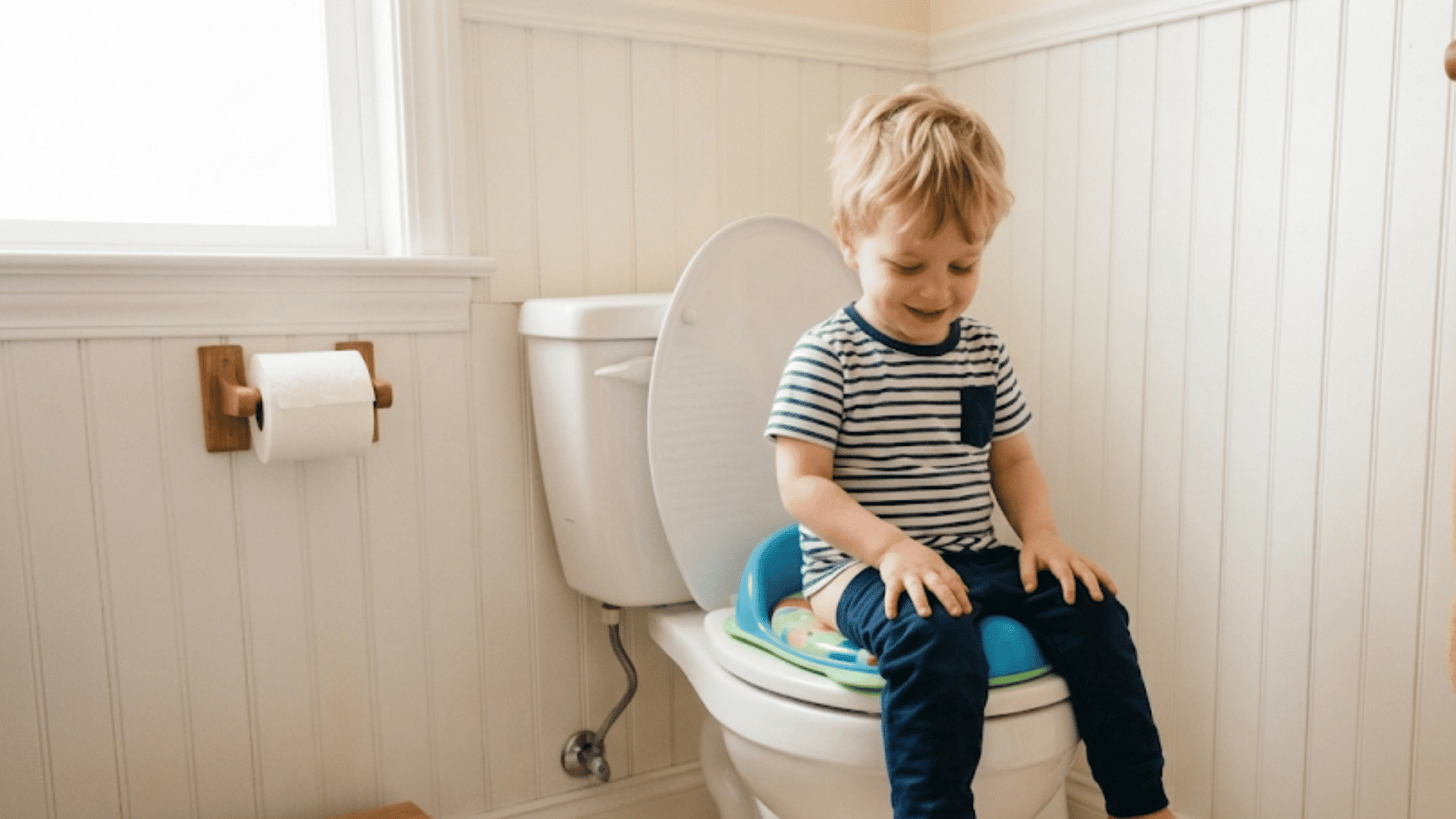 a young boy is smiling and looking down while sitting on a potty seat on top of a standard toilet in a bathroom