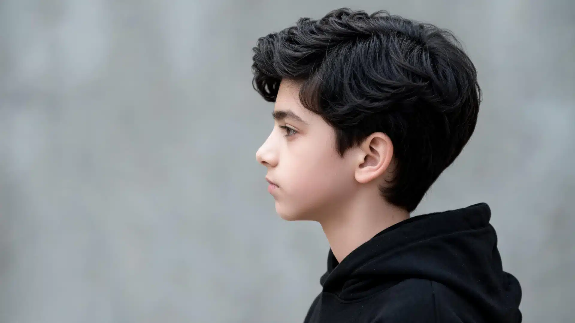 boy with thick side swept straight hair and soft layered volume shown in side profile wearing a black hoodie