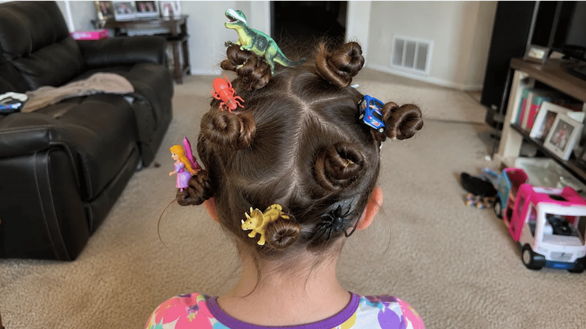 brunette hair with tiny buns holding toy dinosaurs cars and fairy figure