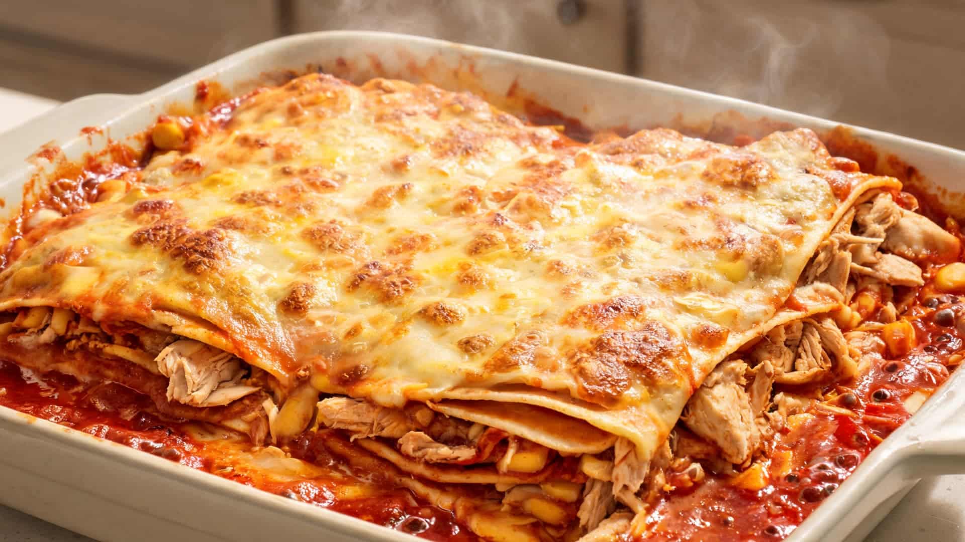 chicken enchiladas with melted cheese topping and red sauce served hot in a baking dish with a warm kitchen