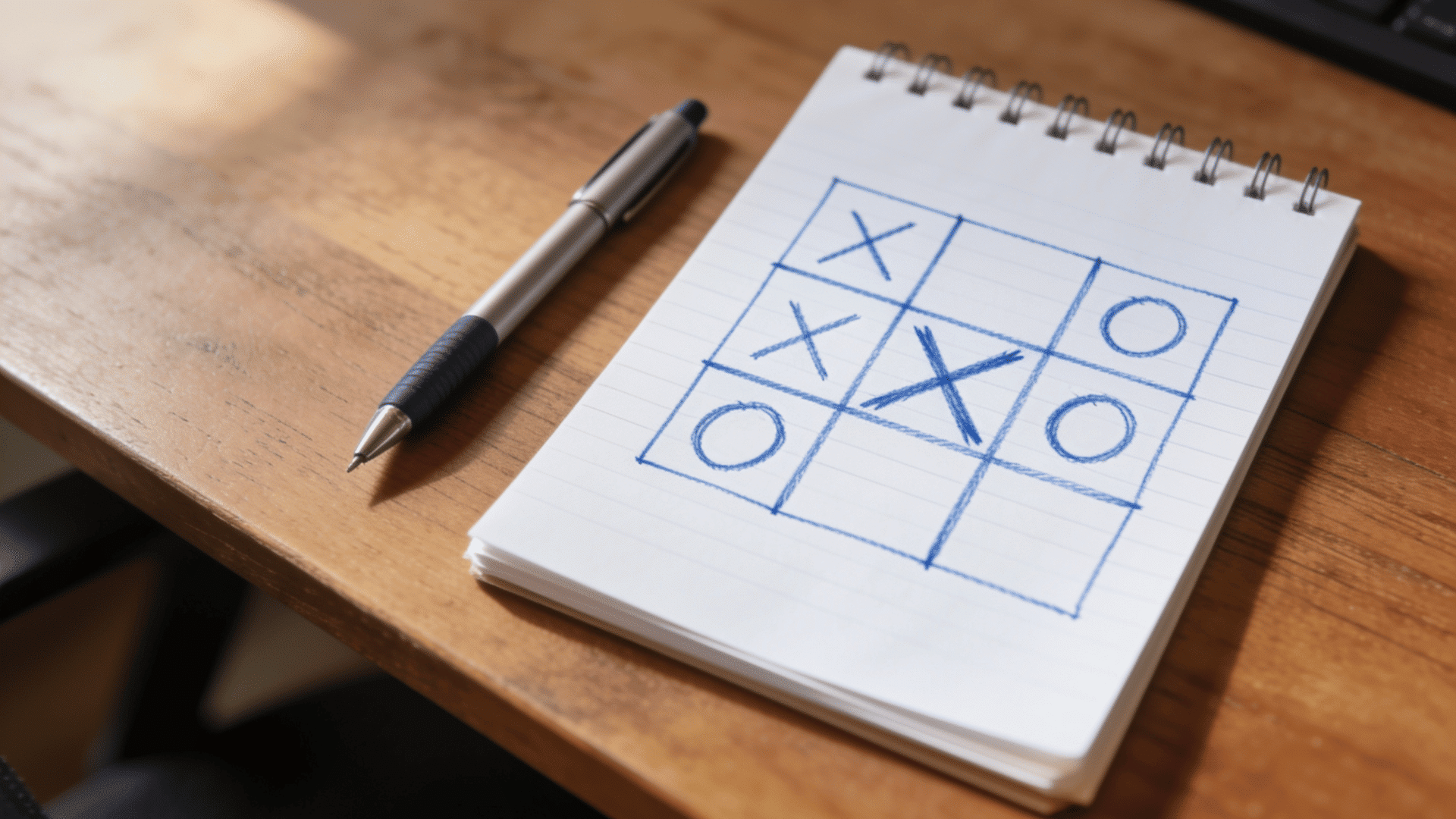 close up spiral notebook with tic tac toe game drawn in blue ink and pen on wooden desk surface with soft light