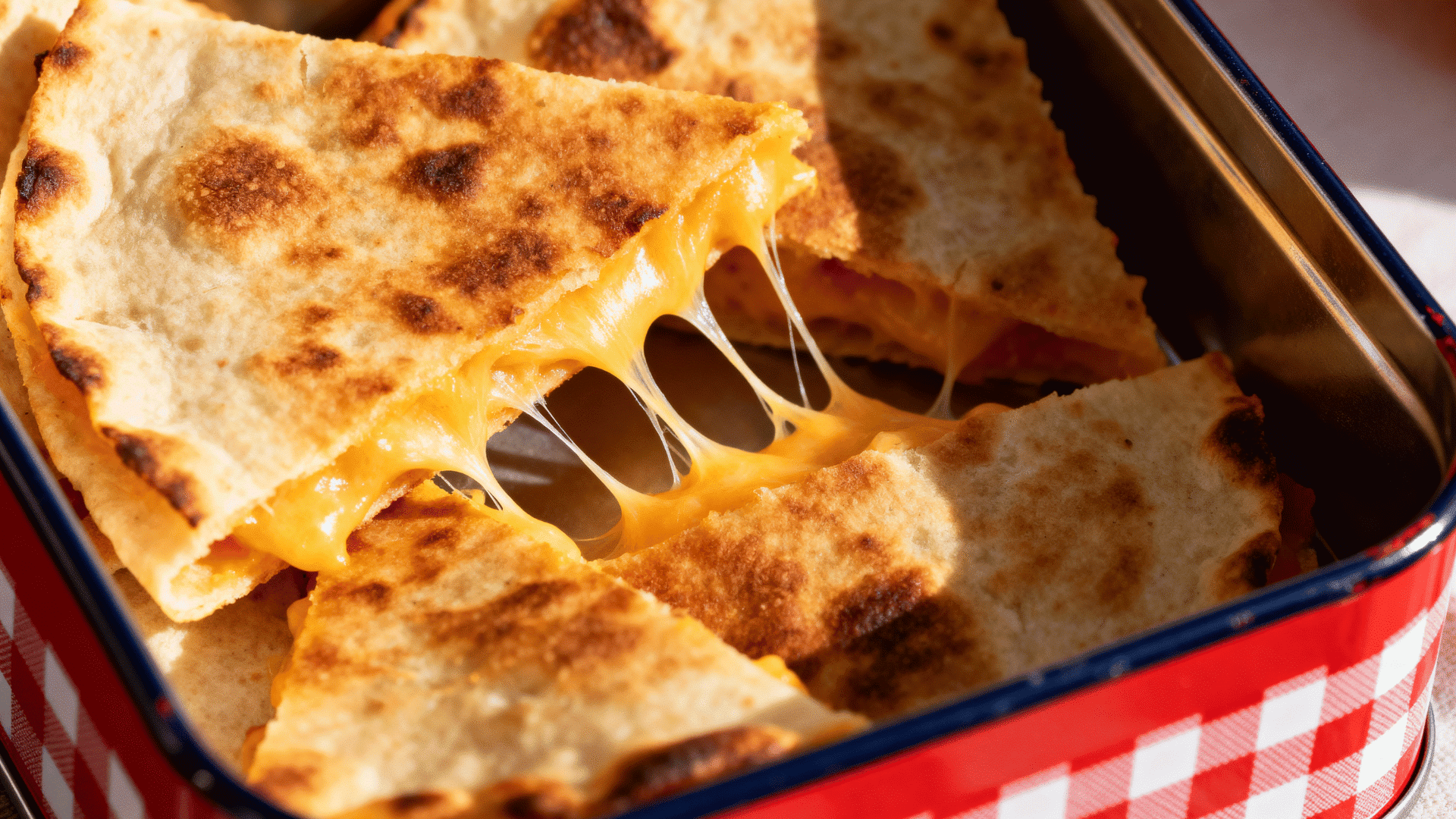 cheesy quesadilla wedges in a red and white checkered enamel lunch tin