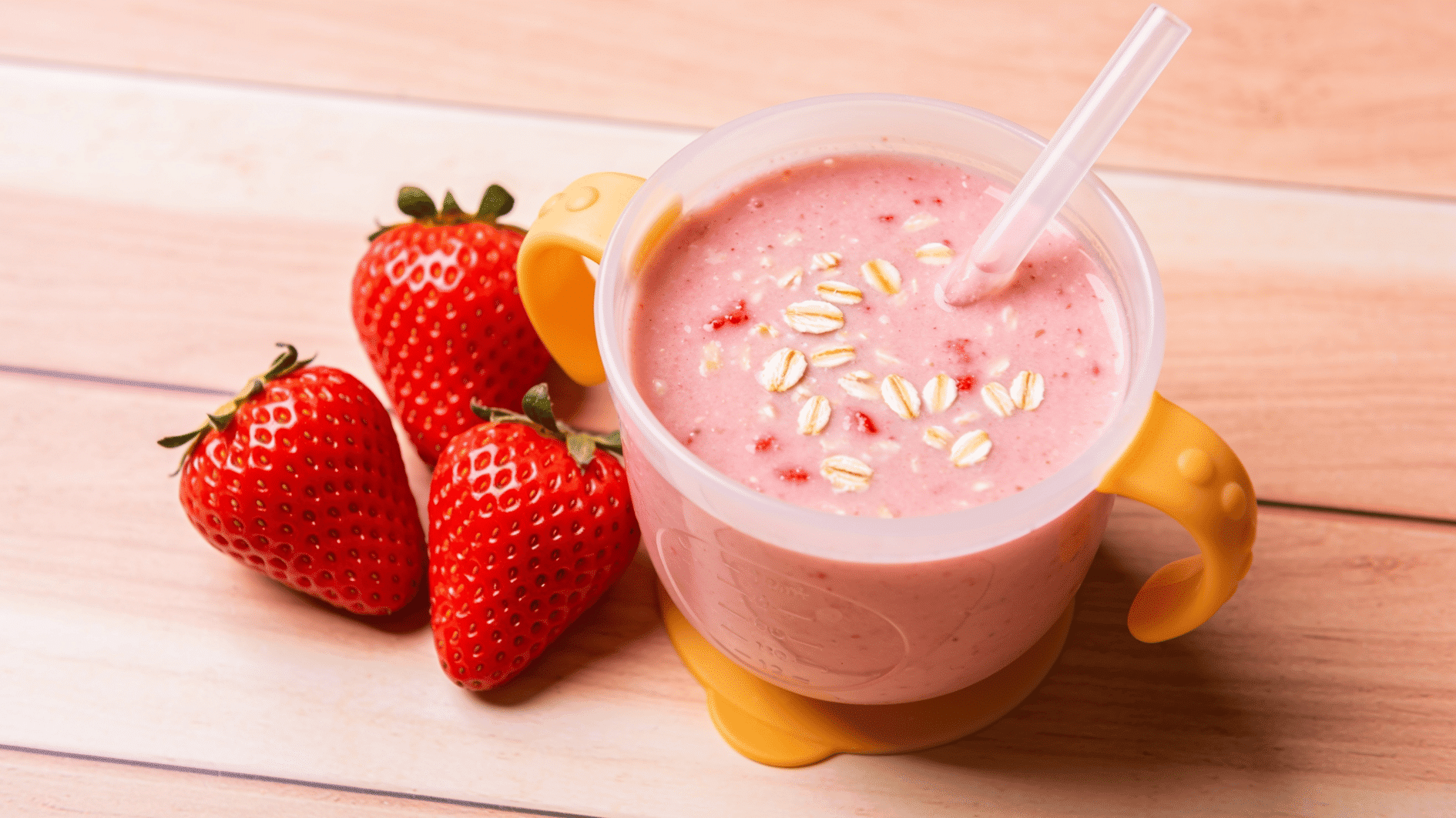 creamy pink strawberry-oat smoothie in a small toddler cup with a straw