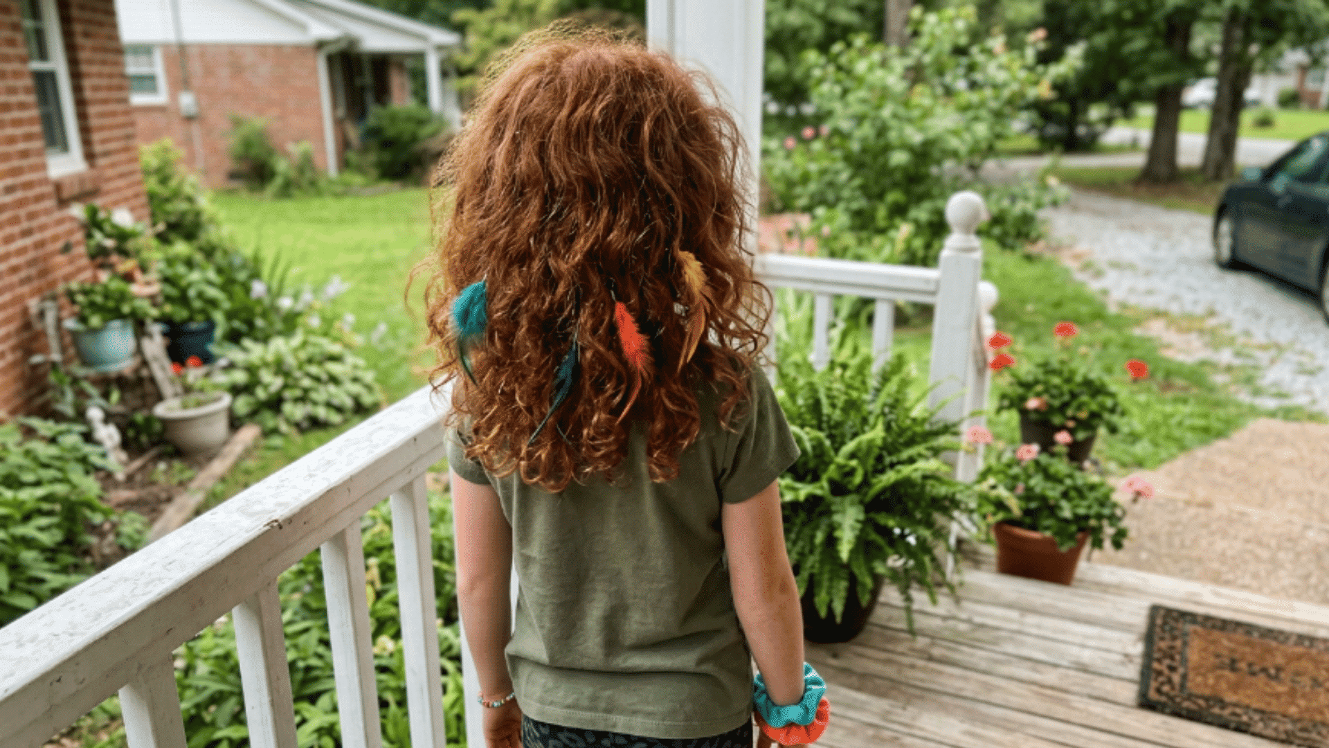 curly auburn hair with teal orange and yellow feather clips on porch railing