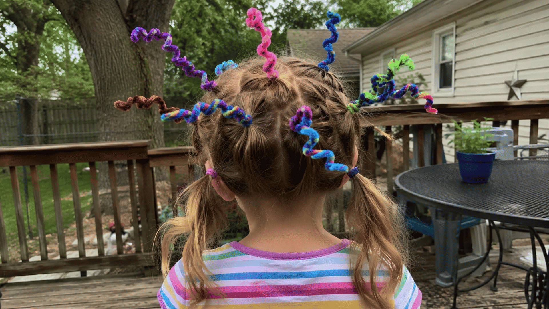 girl with rainbow spiral pipe cleaners twisted into pigtails, outdoor deck, candid crazy hair day photo